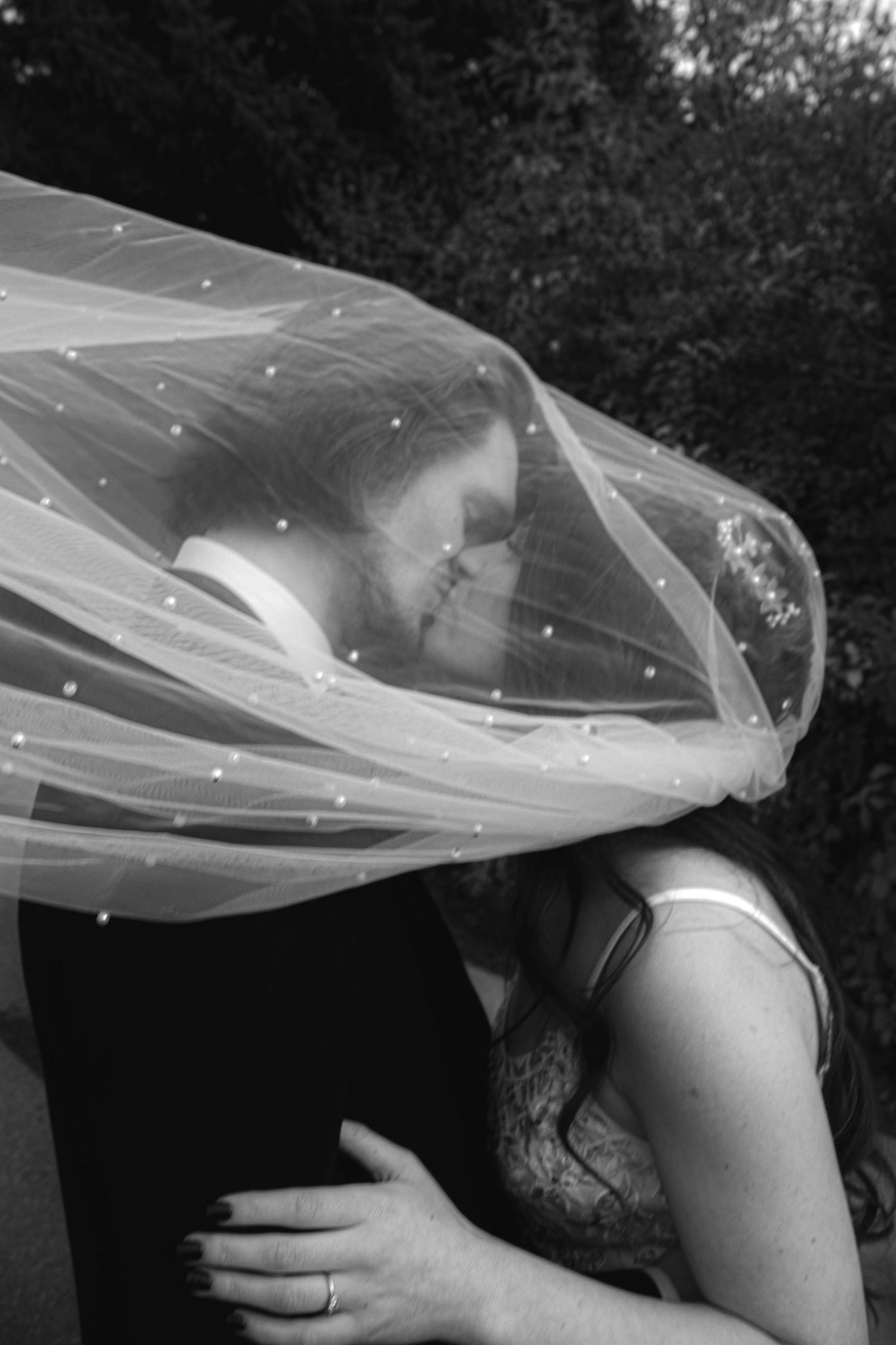 Black and white wedding photo of couple kissing under flowing veil with sparkle details.