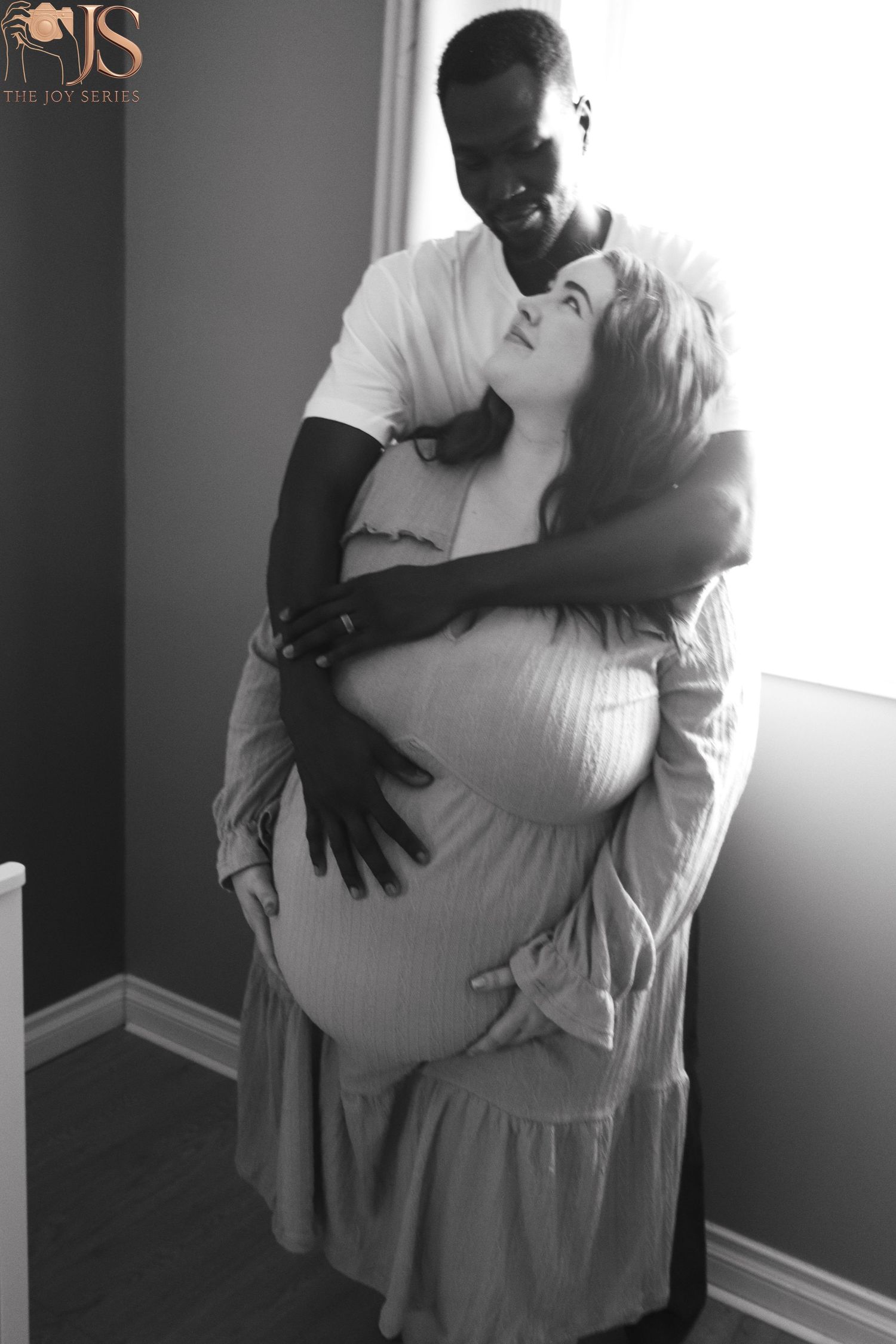 A romantic black and white maternity photo shows a couple embracing, with hands tenderly placed on a pregnant belly.