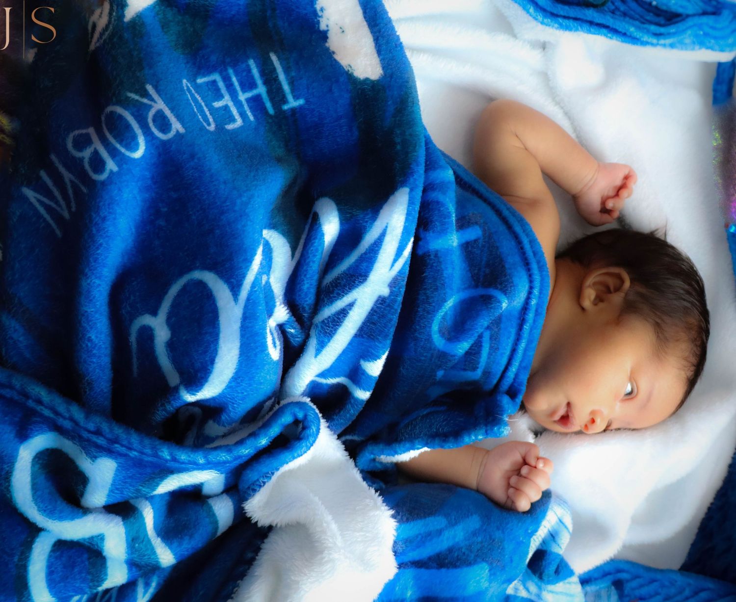 A small person sleeps peacefully under a cozy blue patterned blanket on white bedding.