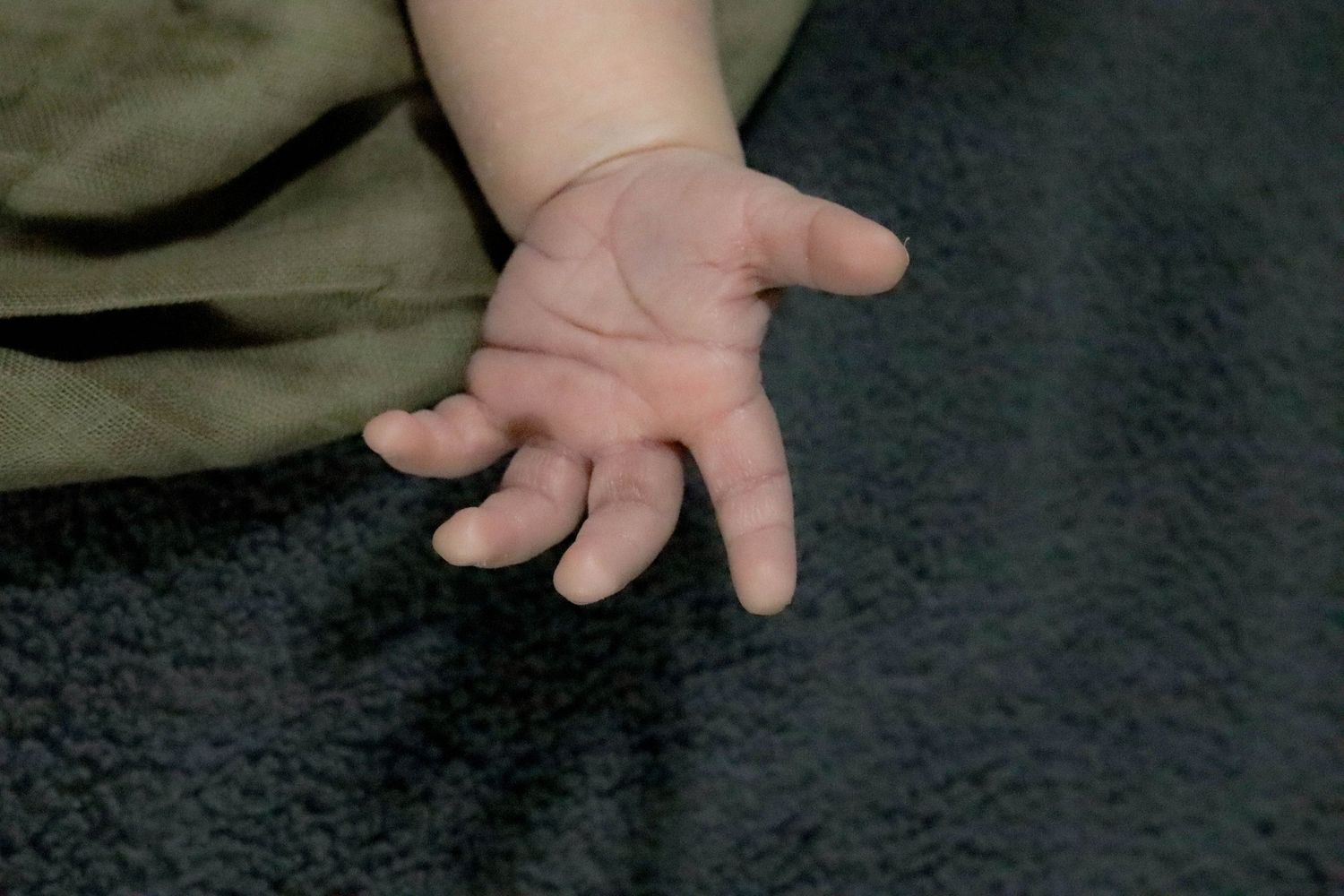 Close-up view of a small baby's hand resting on a dark textured surface.