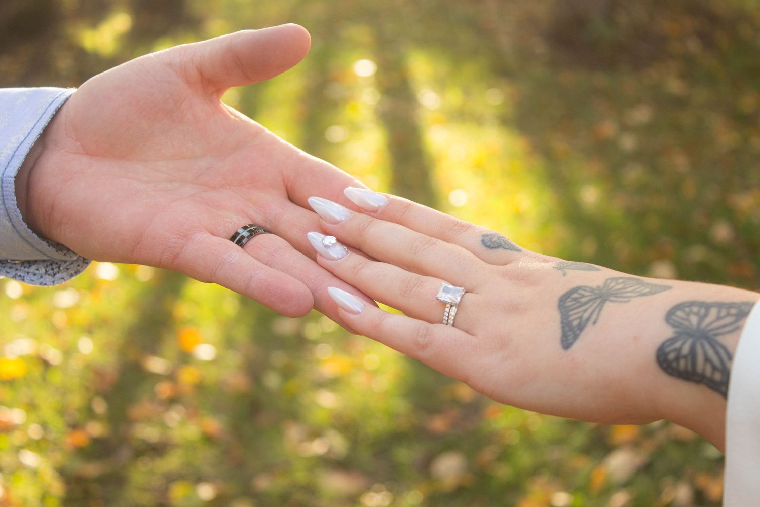 Close-up of two hands showing engagement rings against a golden sunlit background.