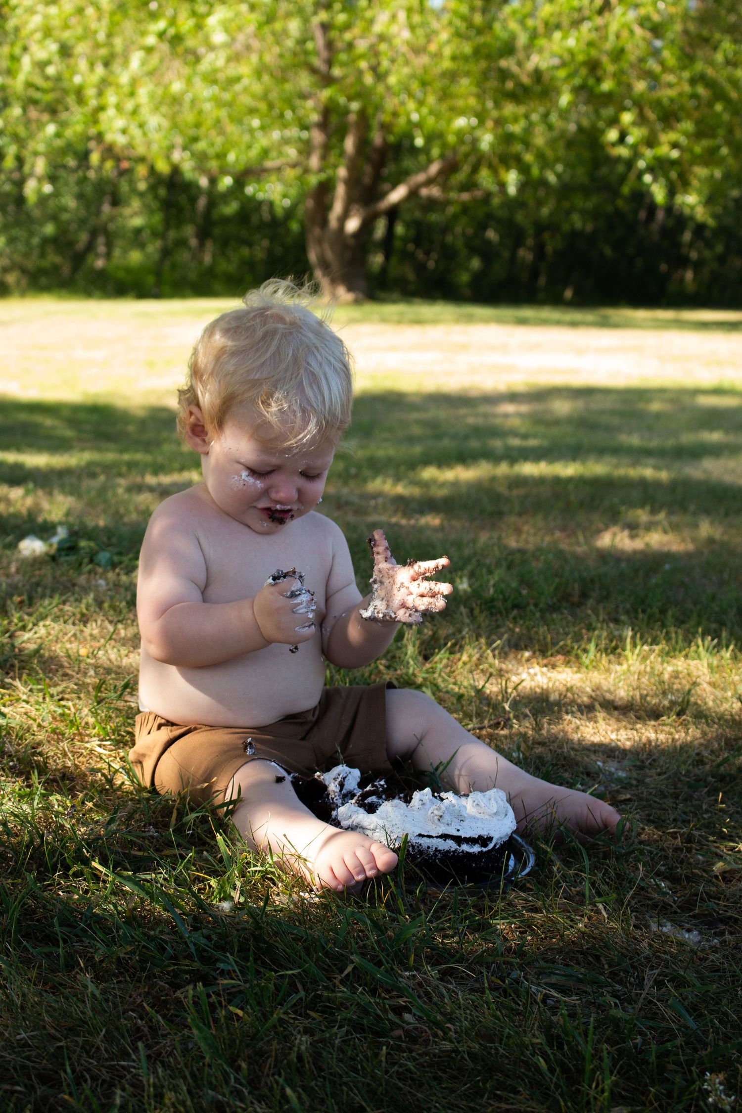 A toddler explores an outdoor setting while sitting on grass with bare feet.