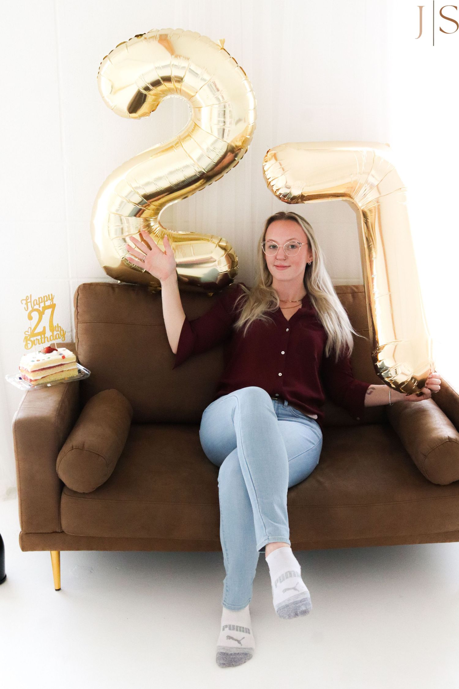 Birthday celebration setup with large gold number 27 balloons and someone relaxing on a brown couch.