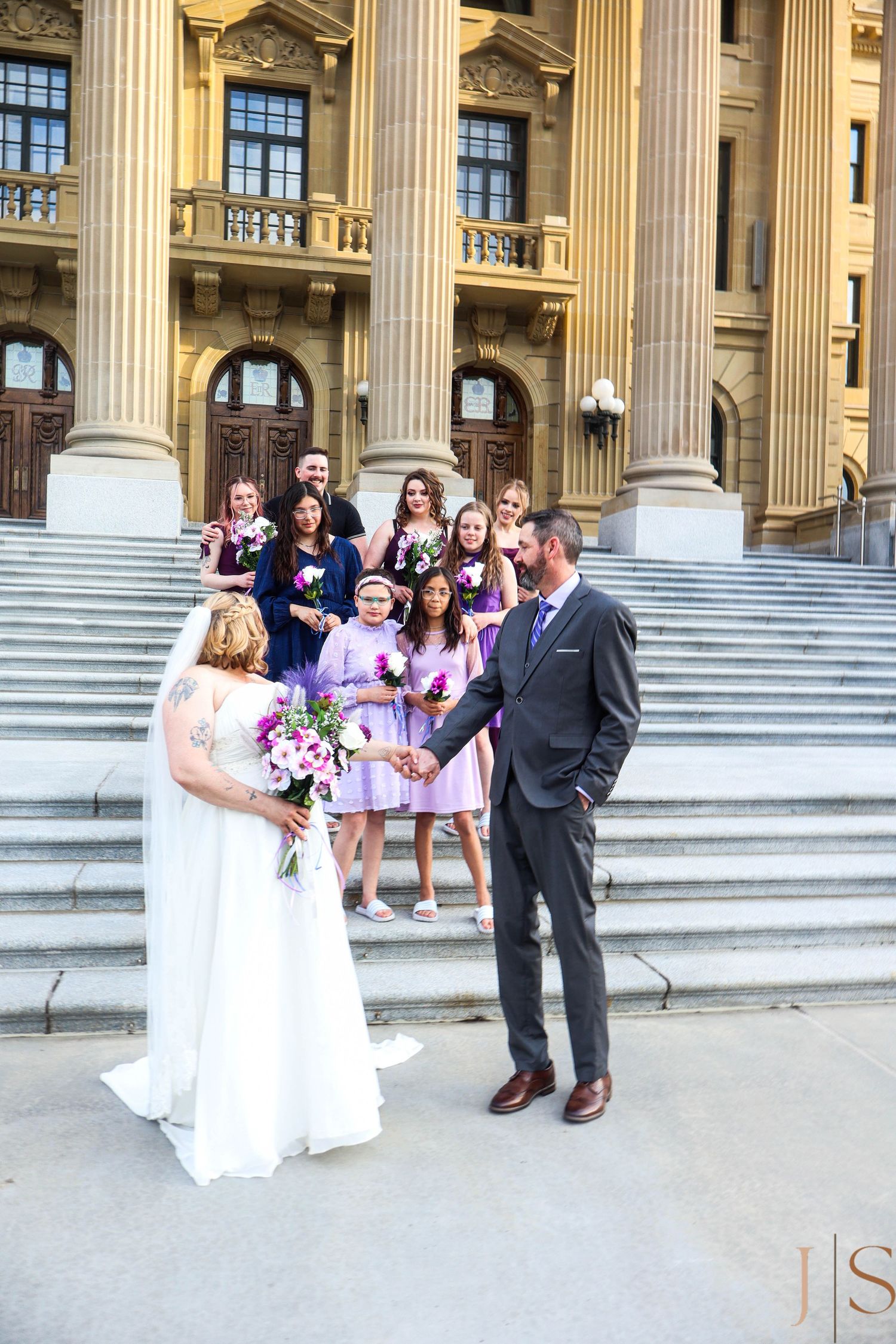 Wedding party gathers on grand courthouse steps with classical columns for formal photo session.
