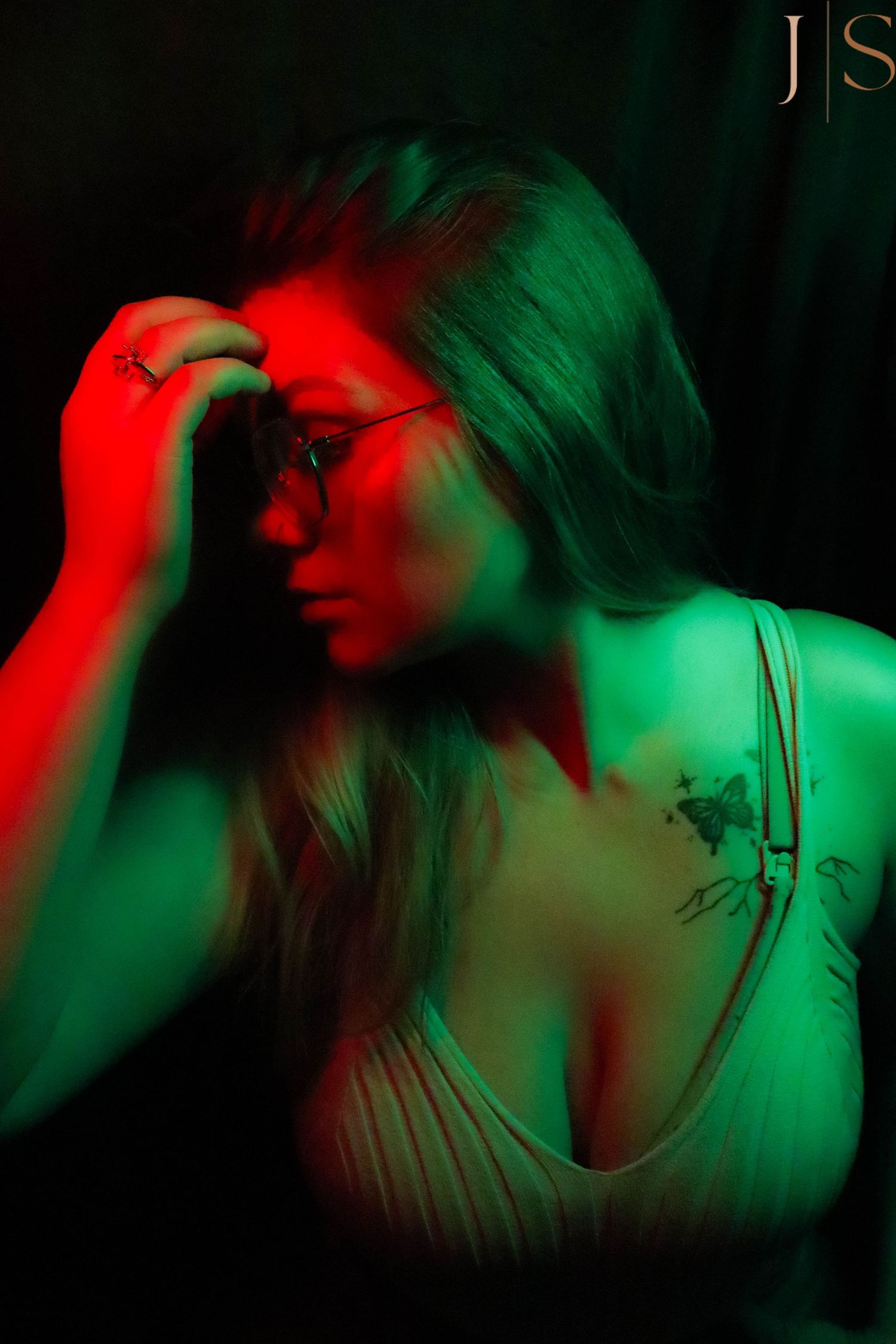 Artistic portrait with dramatic red and green lighting creating moody atmosphere in dark setting.