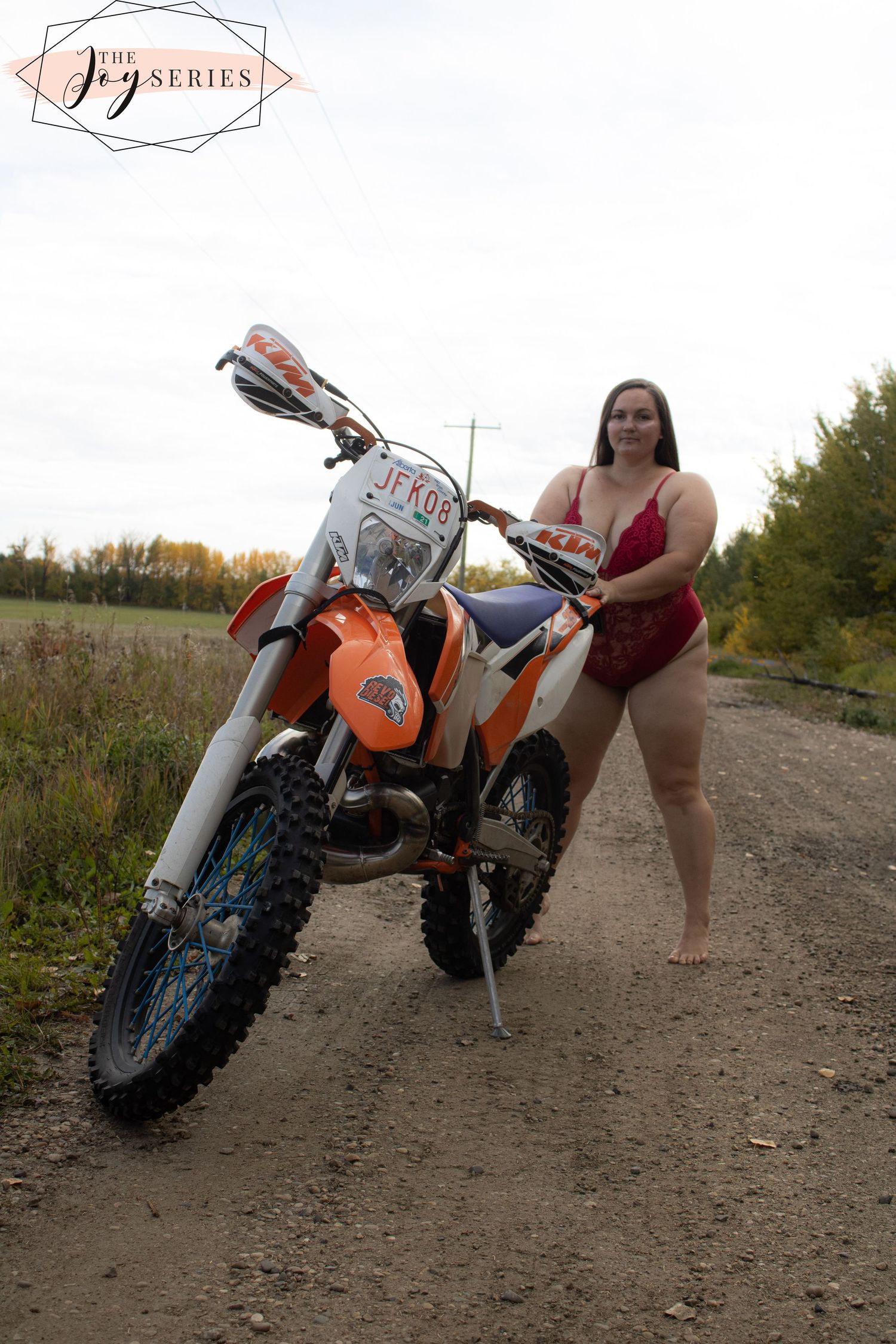 An orange and white KTM dirt bike parked on a dirt trail with autumn foliage in the background.