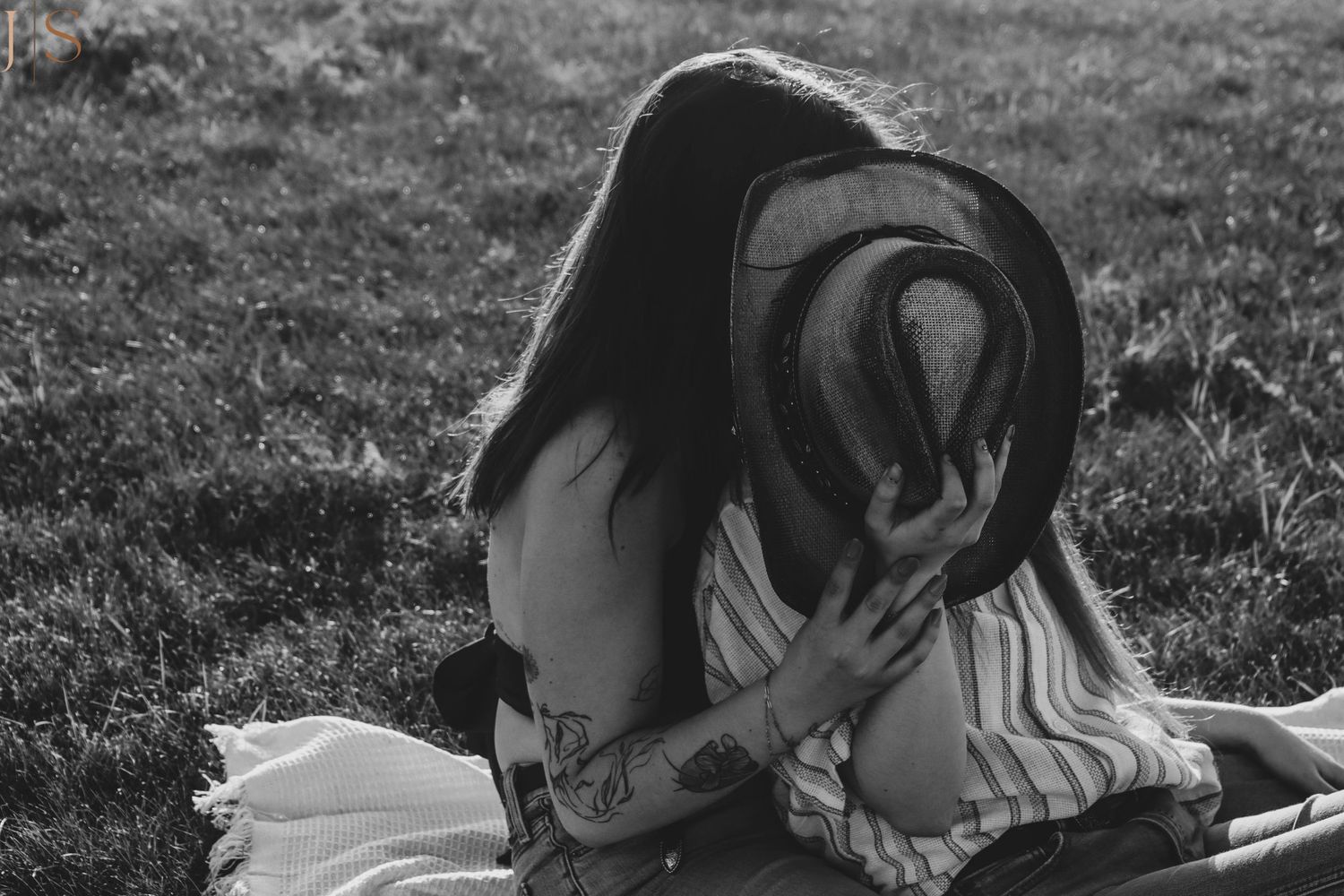 Black and white image of someone wearing a hat laying down on grass while reading a book.