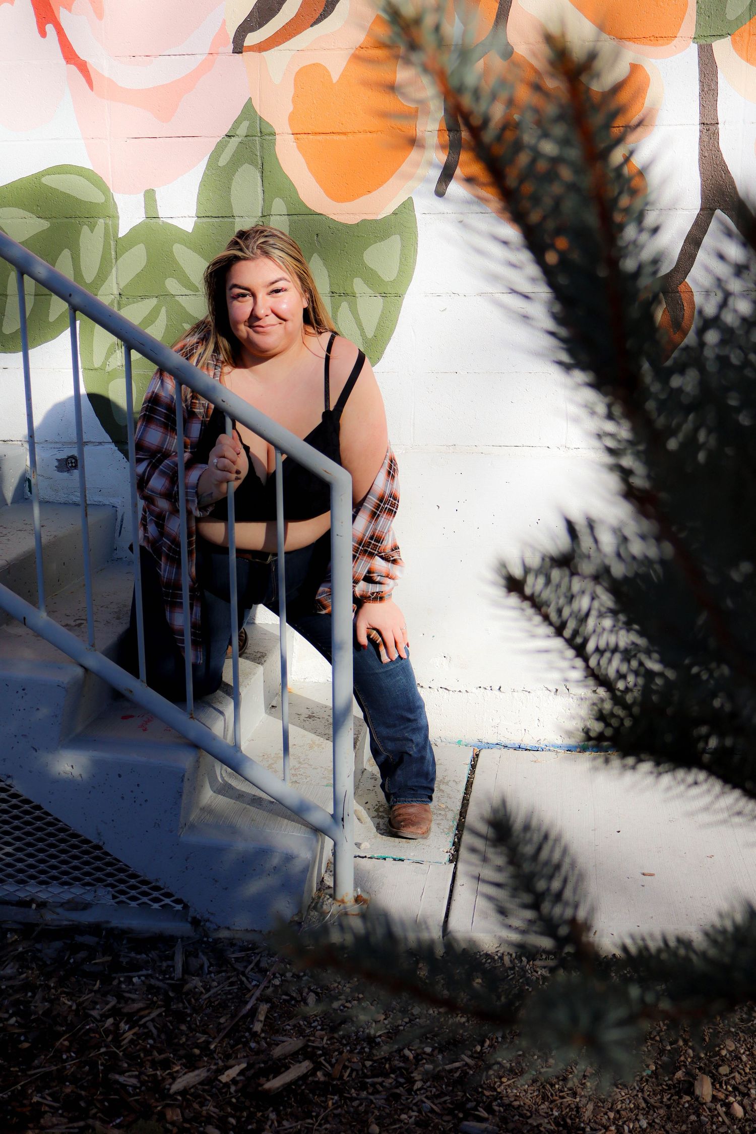 Artistic portrait on stairs with colorful mural and plaid shirt.