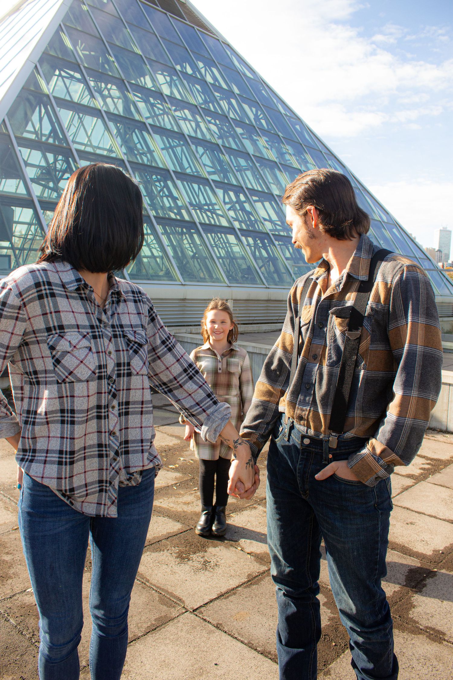 Family stands in front of modern glass pyramid building architecture.