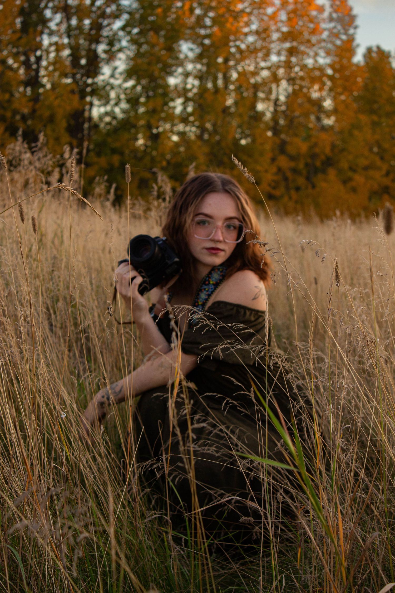 Photographer with a camera poses in tall autumn grass during golden hour.