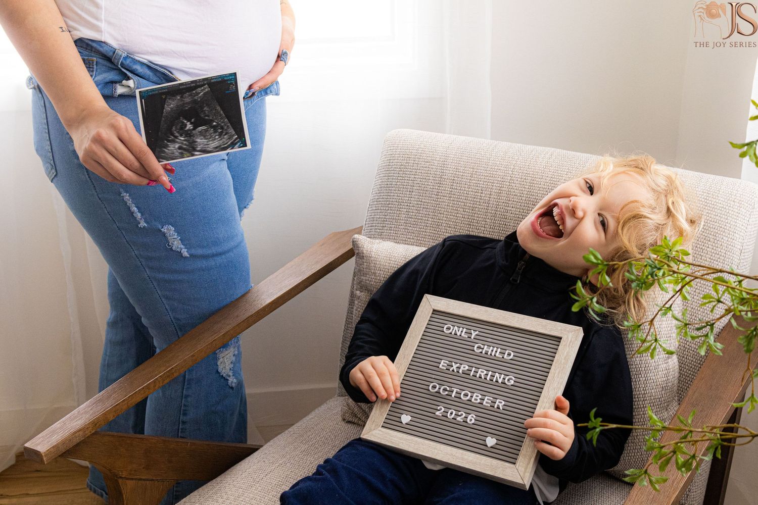 Laughing toddler holds letter board sign reading 'Only Child Expiring October 2026' next to pregnant mom holding ultrasound.