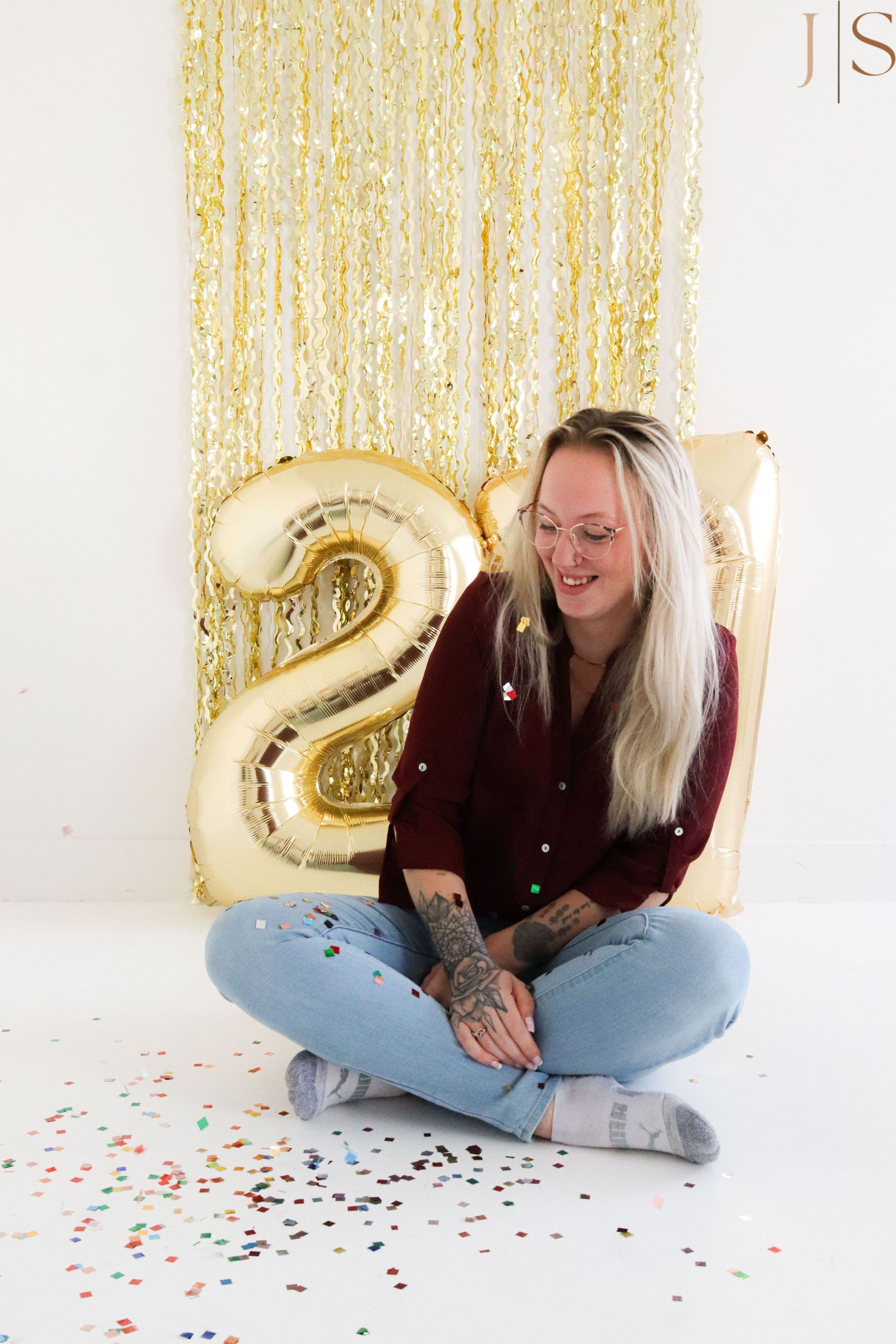 Person sitting cross-legged on floor with gold number 2 balloon and sparkly backdrop.