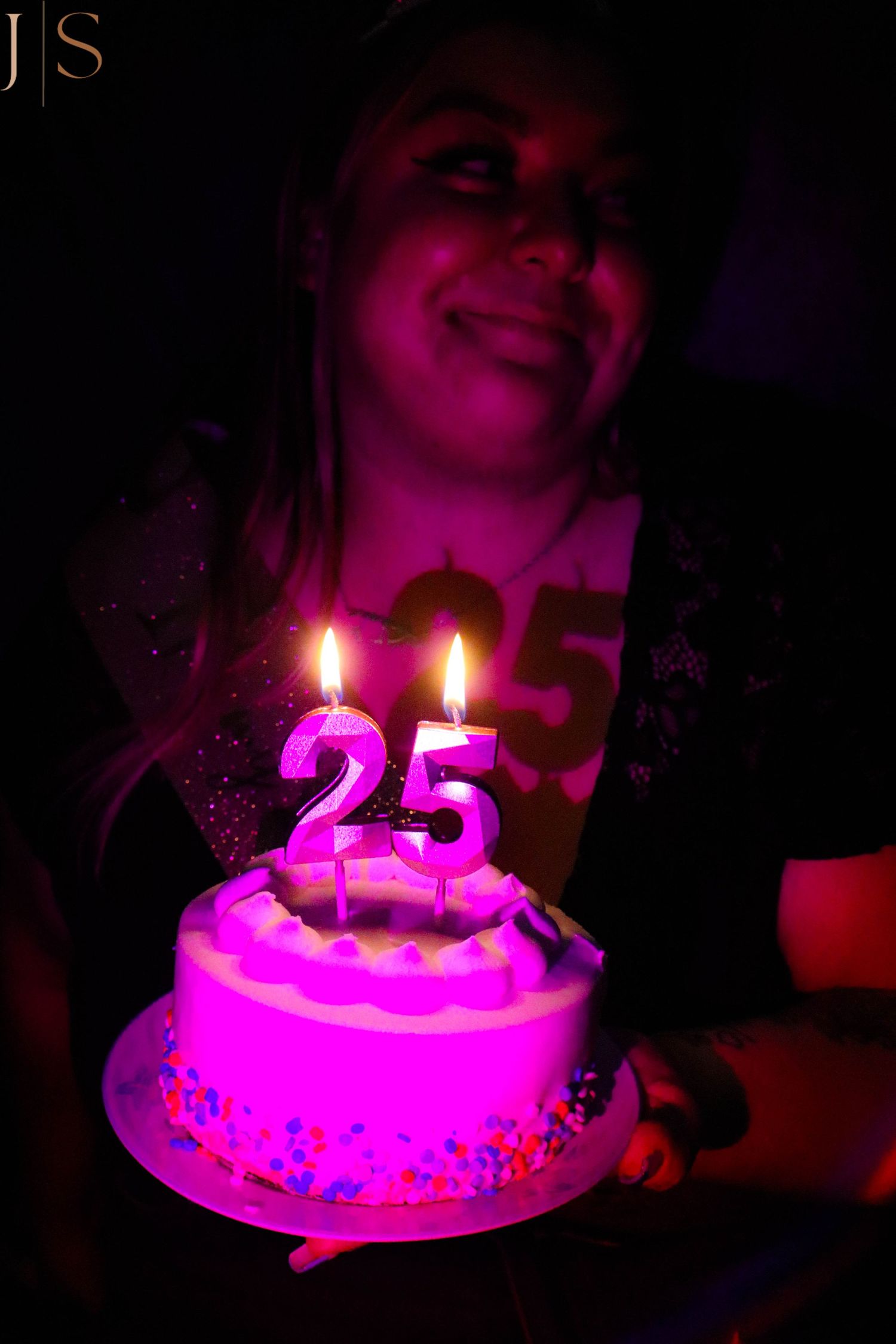 Birthday celebration with lit number 25 candles on a pink-illuminated cake.