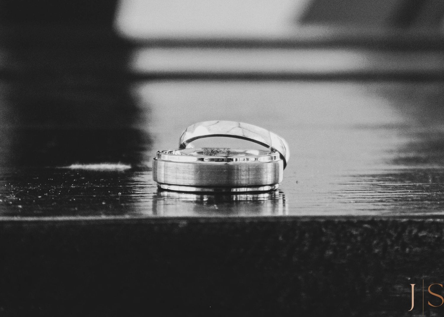 Wedding rings captured in dramatic black and white close-up on a reflective surface.