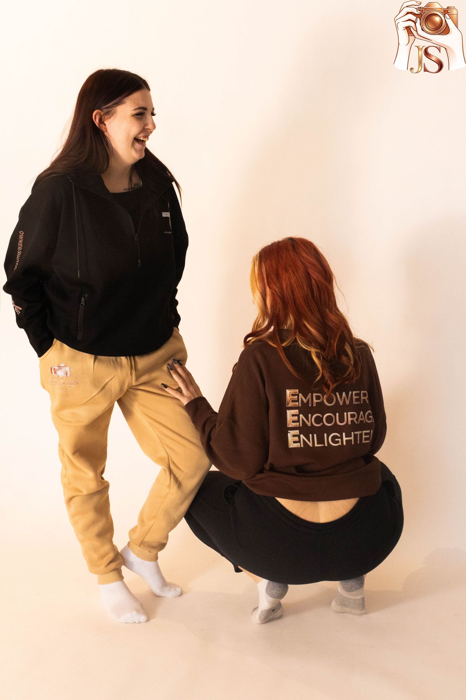 Two people wearing black and yellow outfits crouch and interact playfully in a studio setting against a light background.