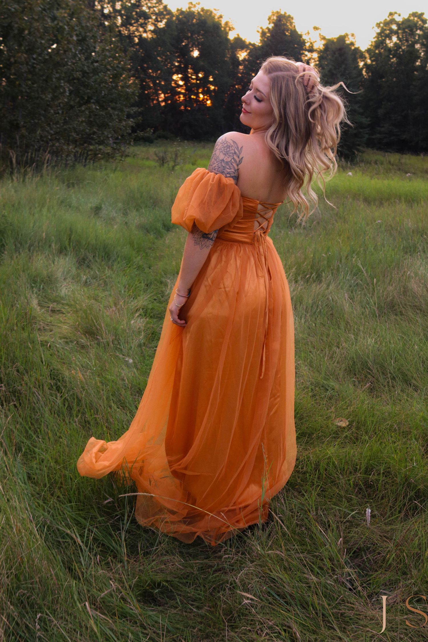 A flowing orange dress creates movement in a golden field during sunset.