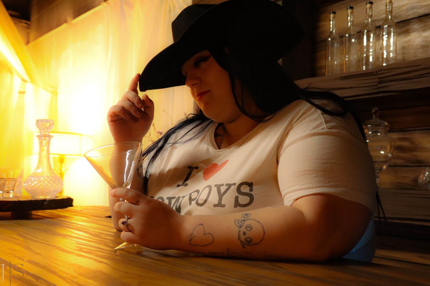 A person wearing a black hat sits at a wooden bar counter in warm lighting.