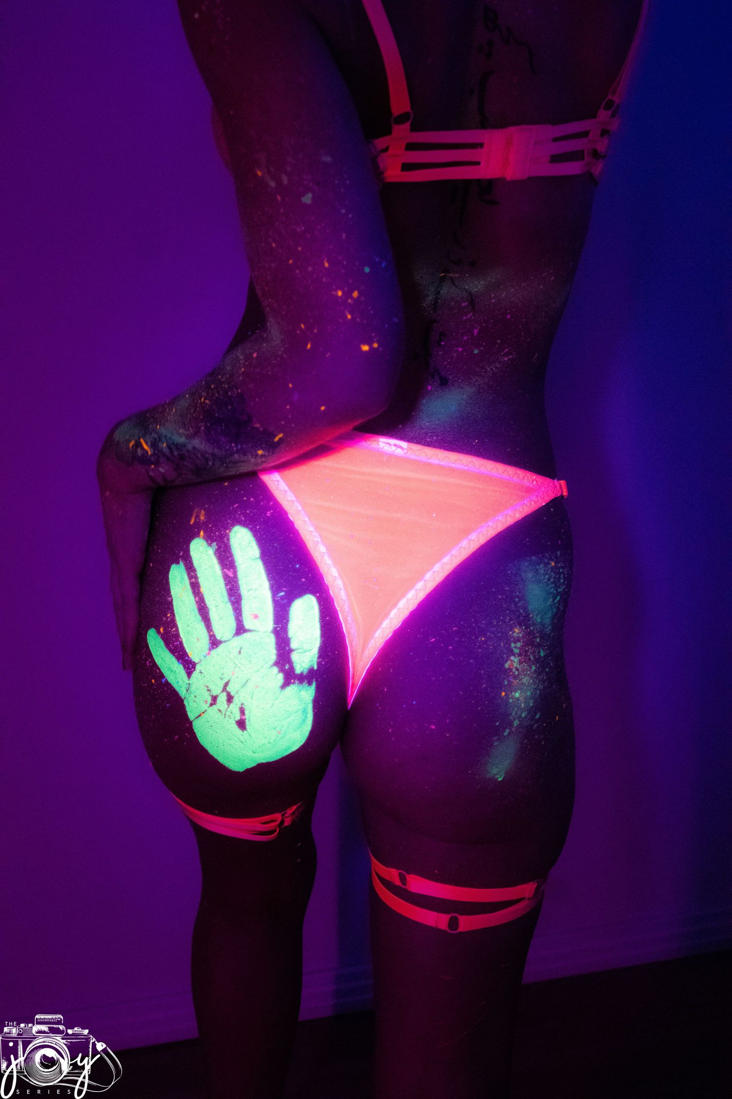 Glowing neon body art featuring a luminescent hand print on skin under blacklight with pink and purple lighting effects.