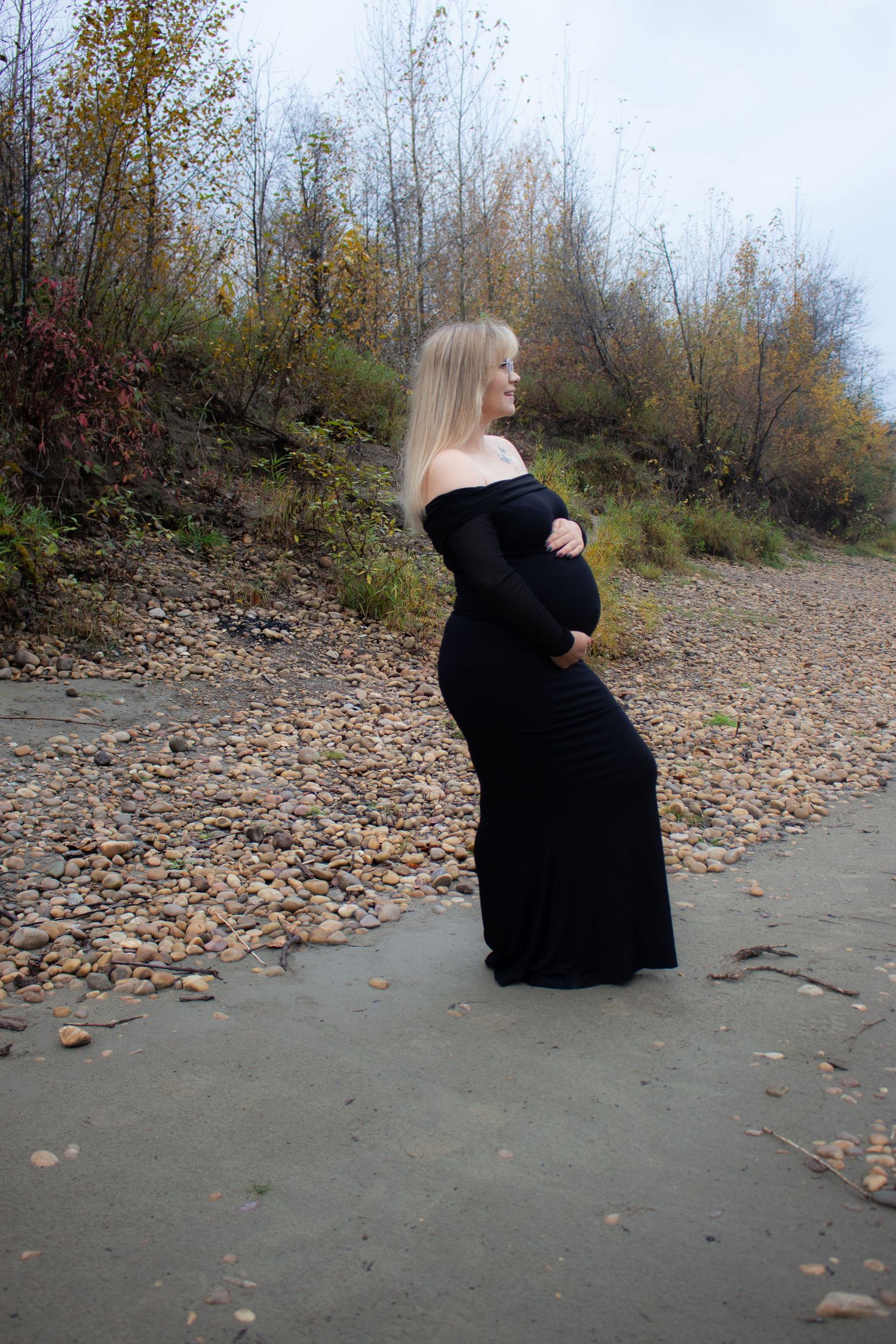 Maternity photo with long black dress against autumn forest backdrop.