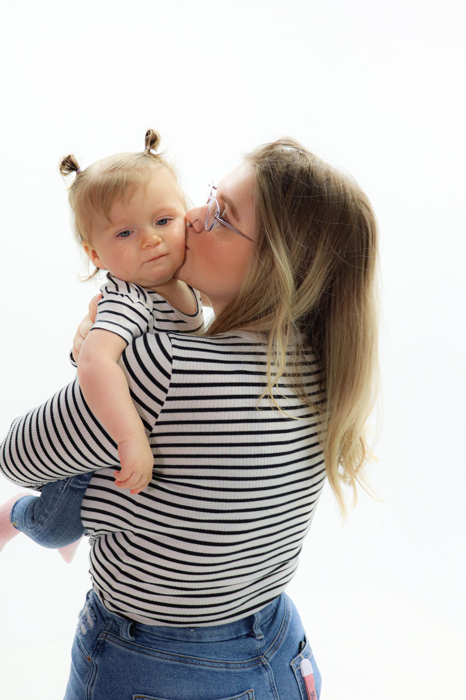 Sweet moment captured as parent in striped shirt kisses small child.