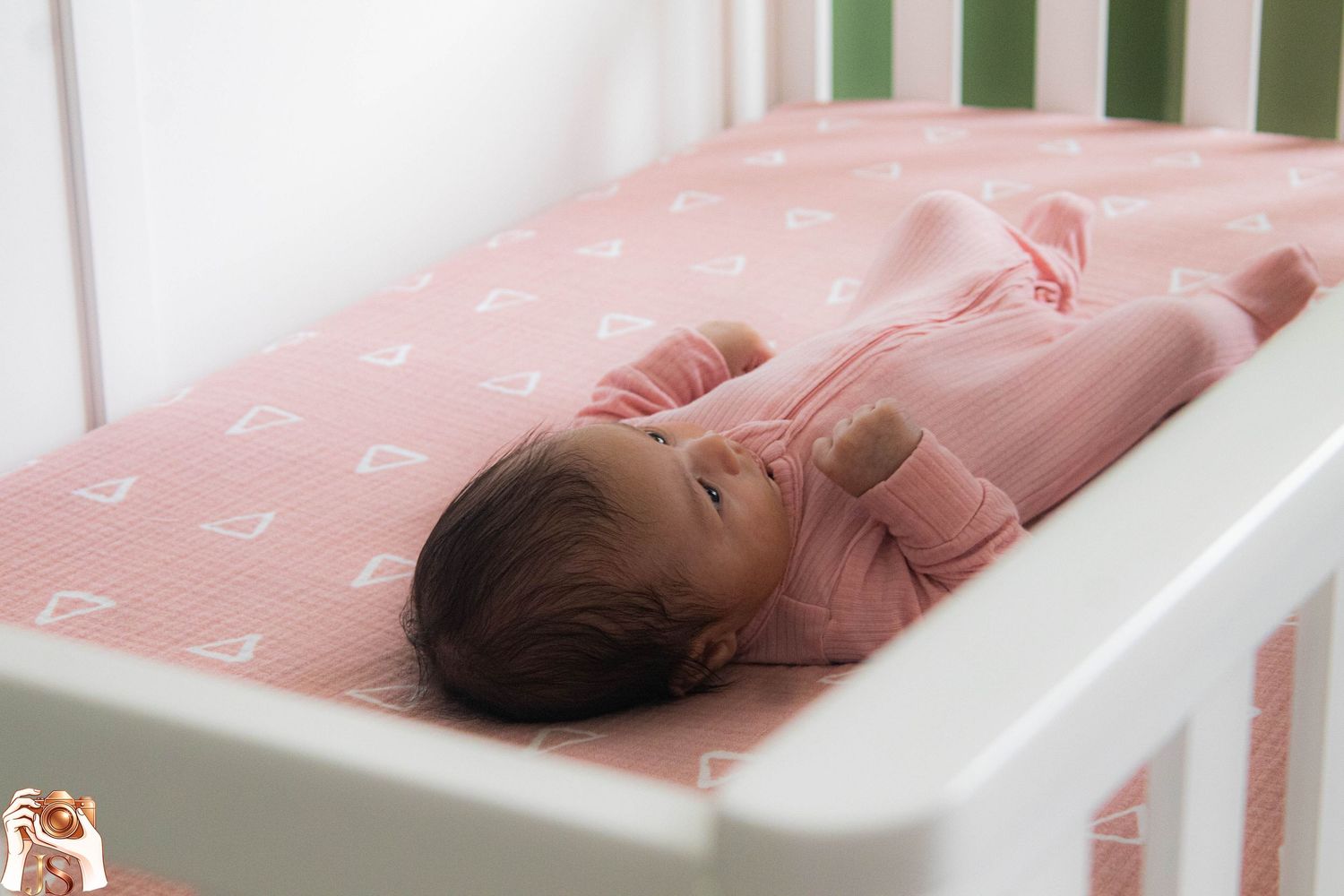 Newborn baby wearing pink sleeps peacefully in white crib with matching bedding.