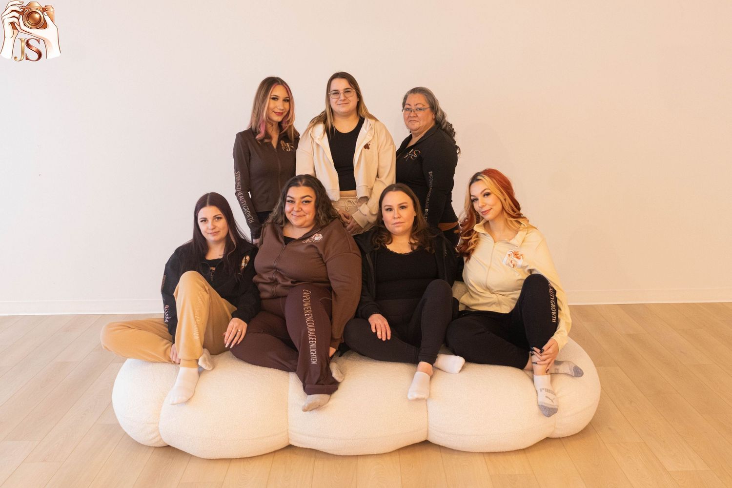 A group of people sit casually together on white bean bag chairs in a minimalist room with wooden floors.