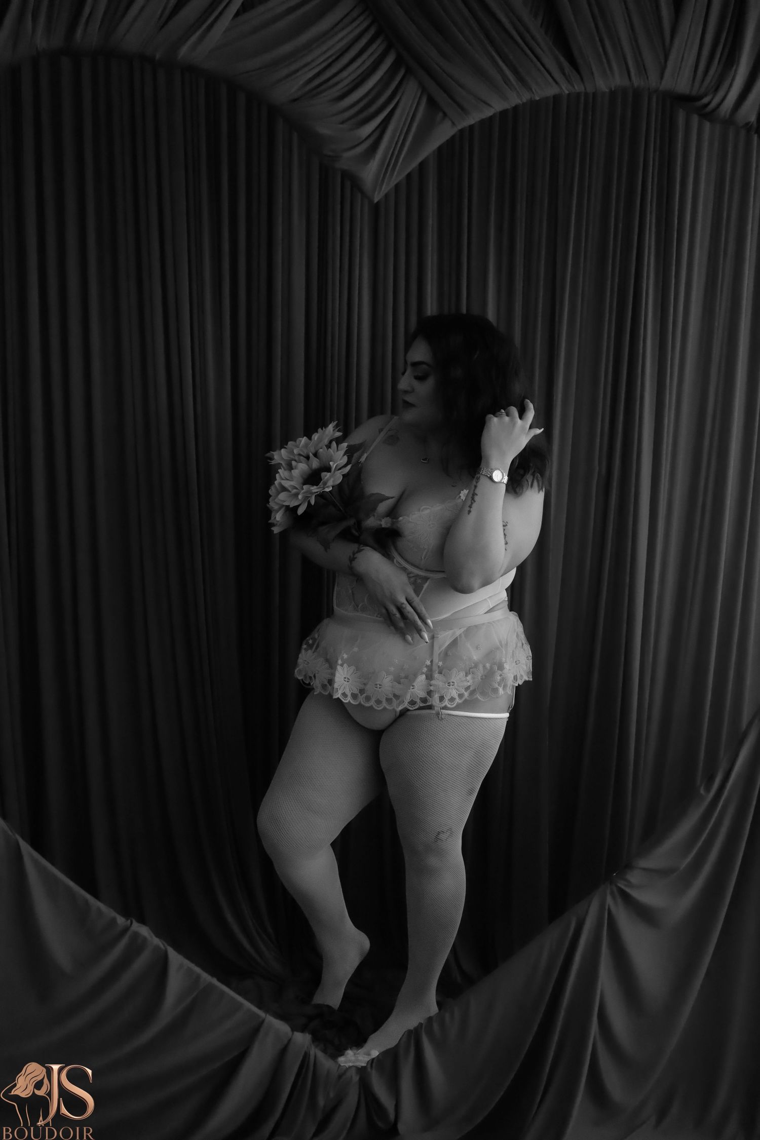 Black and white boudoir photo with draped fabric backdrop and floral bouquet.