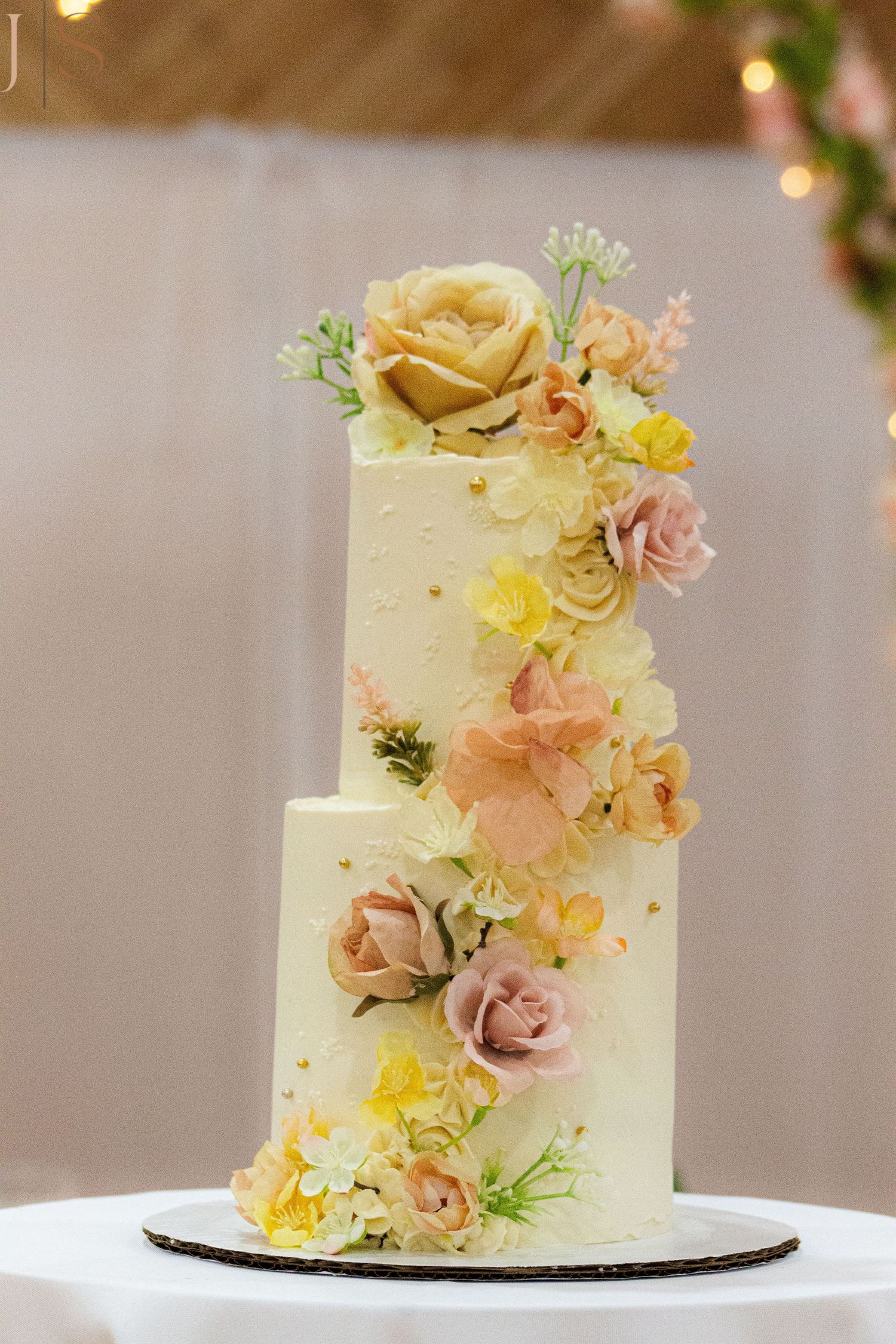 Elegant white wedding cake decorated with delicate yellow and pink flowers in a romantic garden style.