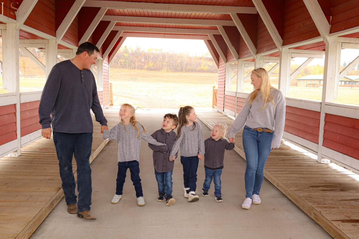 A group of people walk through a covered wooden bridge with red painted walls and white trim details.