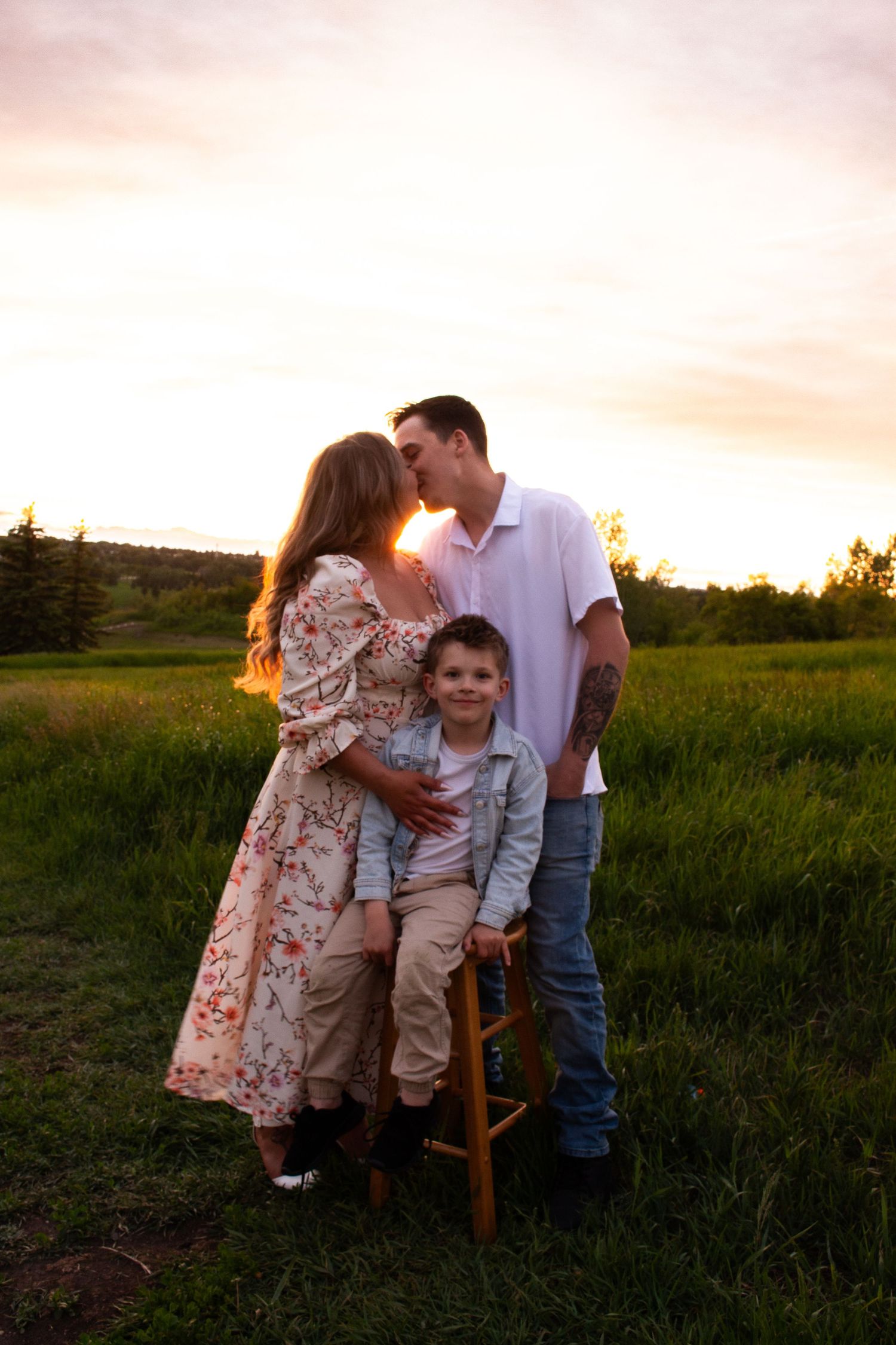Family portrait at golden hour in countryside with wooden stool.