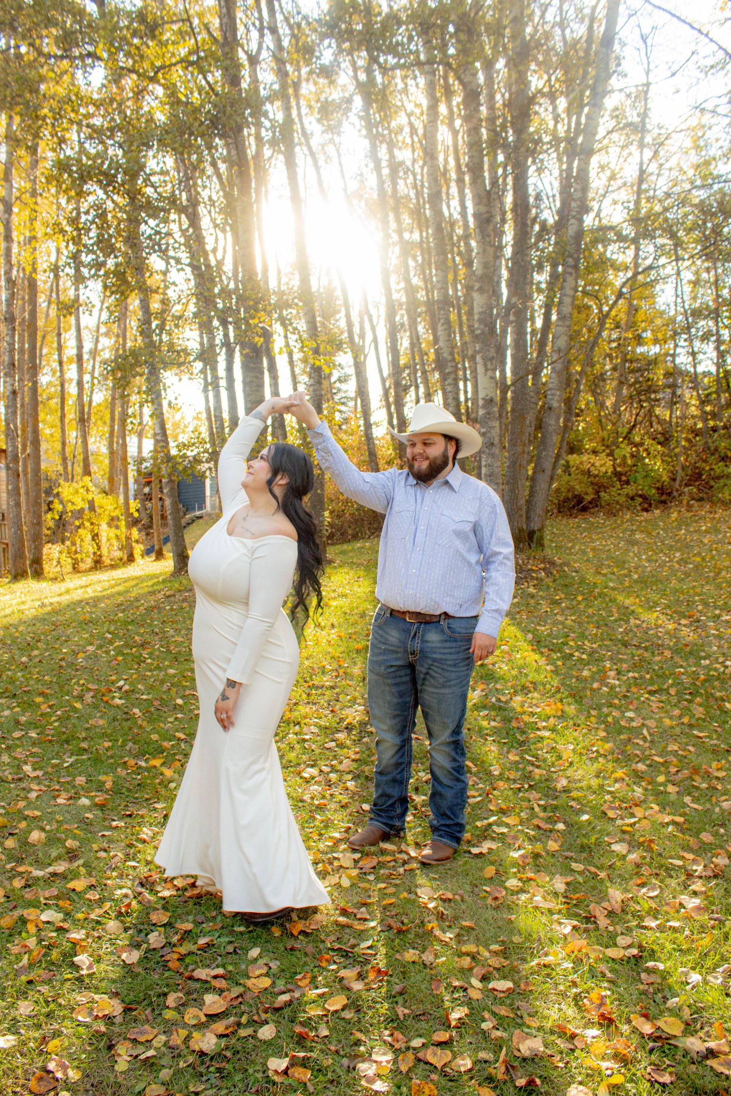 Couple dancing in autumn forest with golden sunlight streaming through trees.
