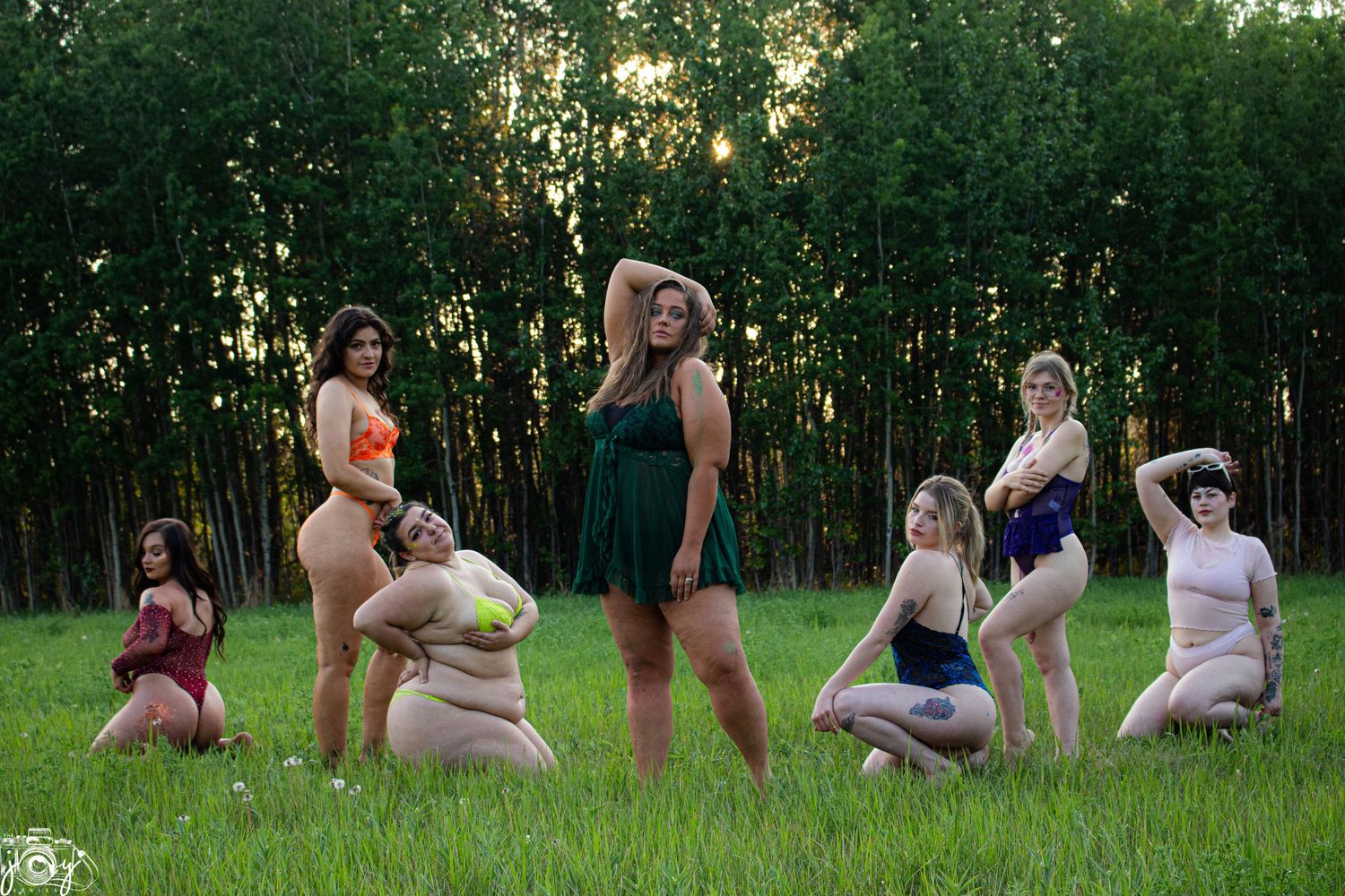 A group of people pose together on grass with trees in the background at sunset.
