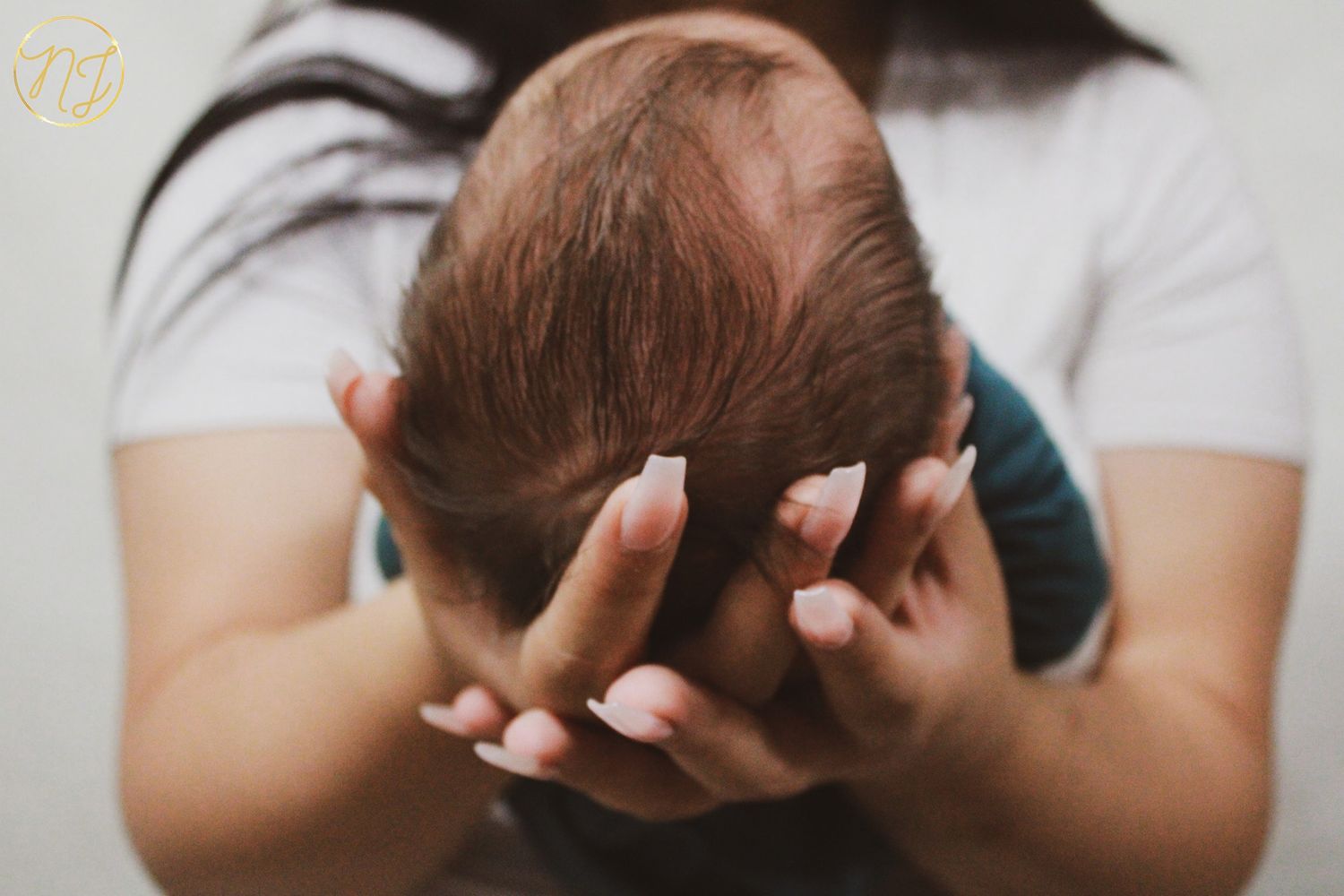 Gentle hands cradle a newborn baby's head against a blurred background.