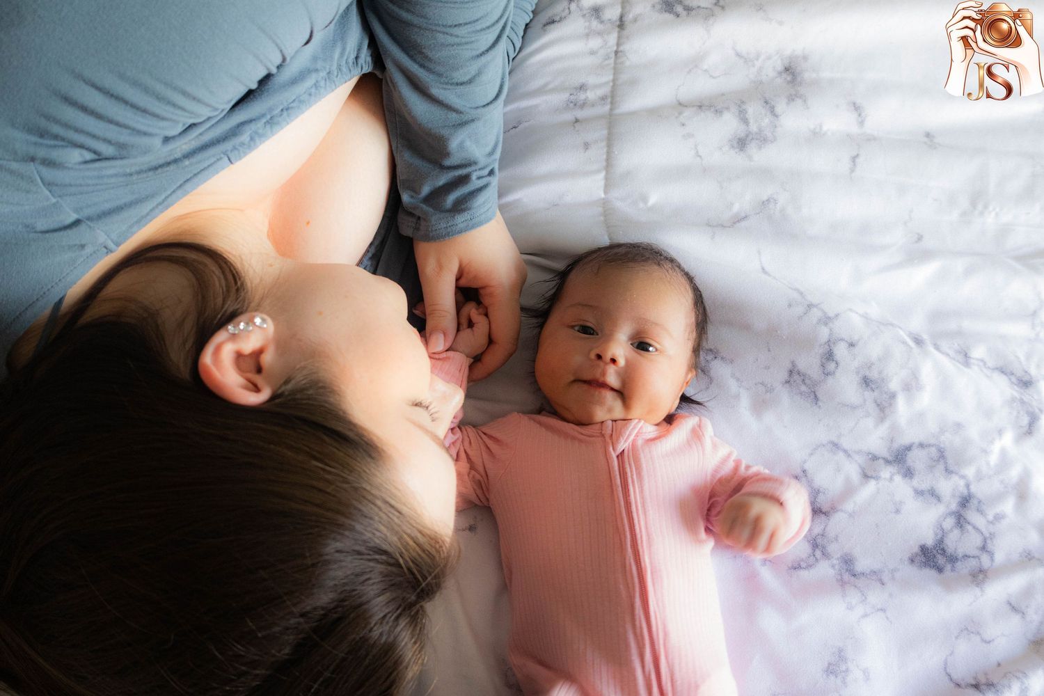 A tender moment captured between parent and infant lying together on white bedding.