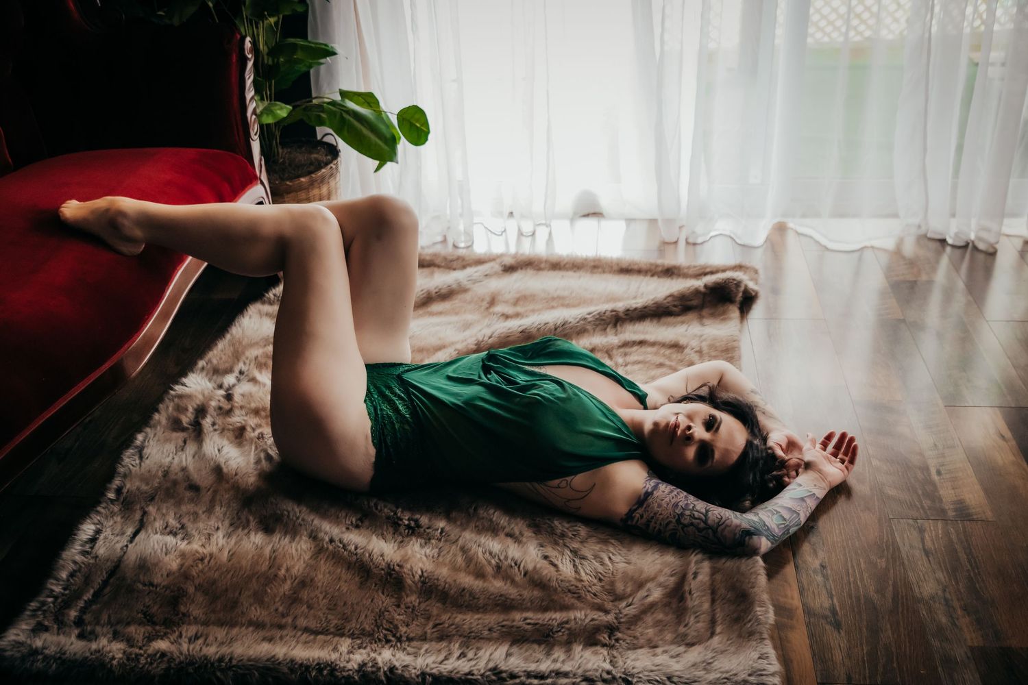Person in a green outfit lying on hardwood floor next to window with natural light streaming in.