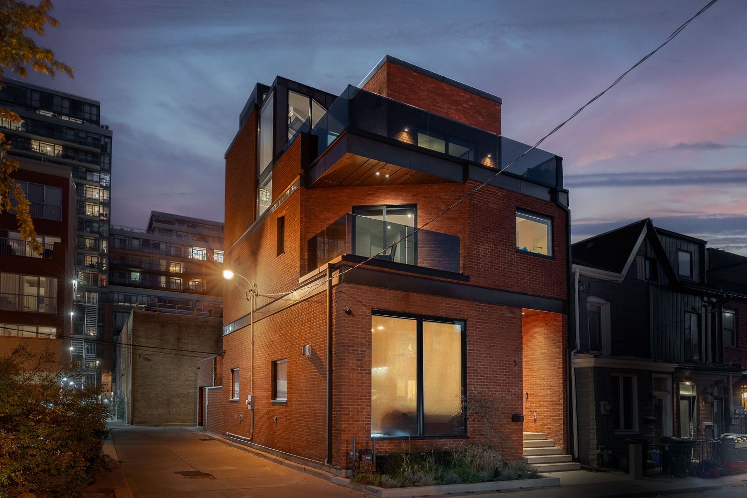 Modern townhouse exteriors with brick facades and large windows illuminate warmly against a dusky evening sky.