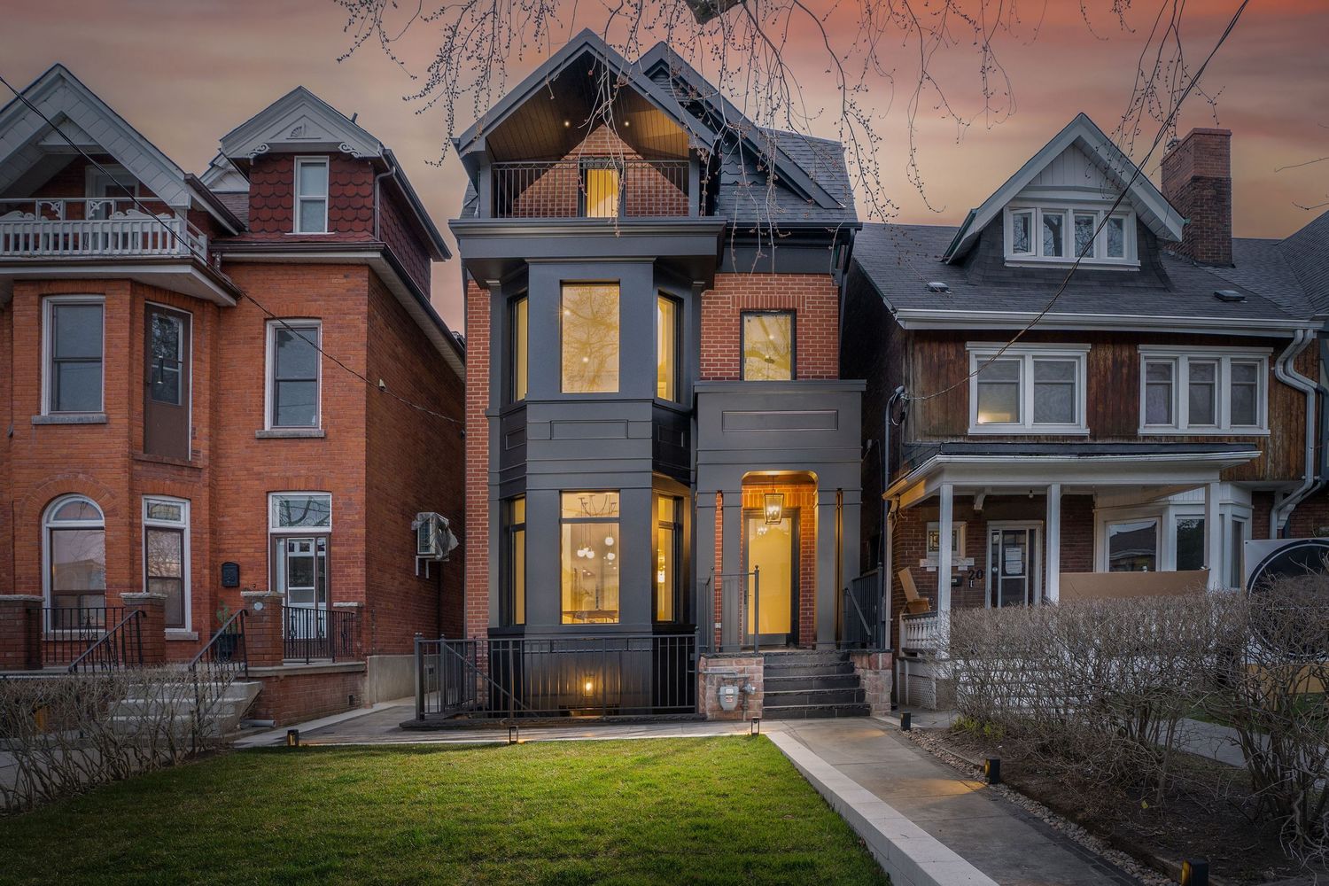 Row of illuminated Victorian style houses with warm glowing windows at sunset on a residential street.