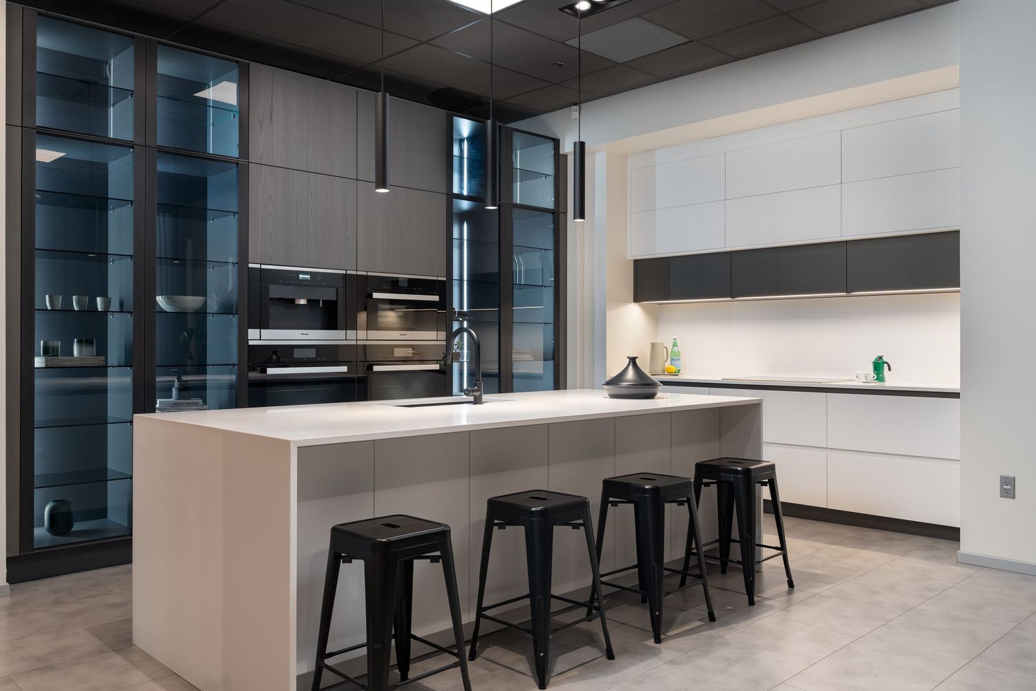 Modern office space with sleek black bar stools along a white counter and glass walls creating an open workspace environment.