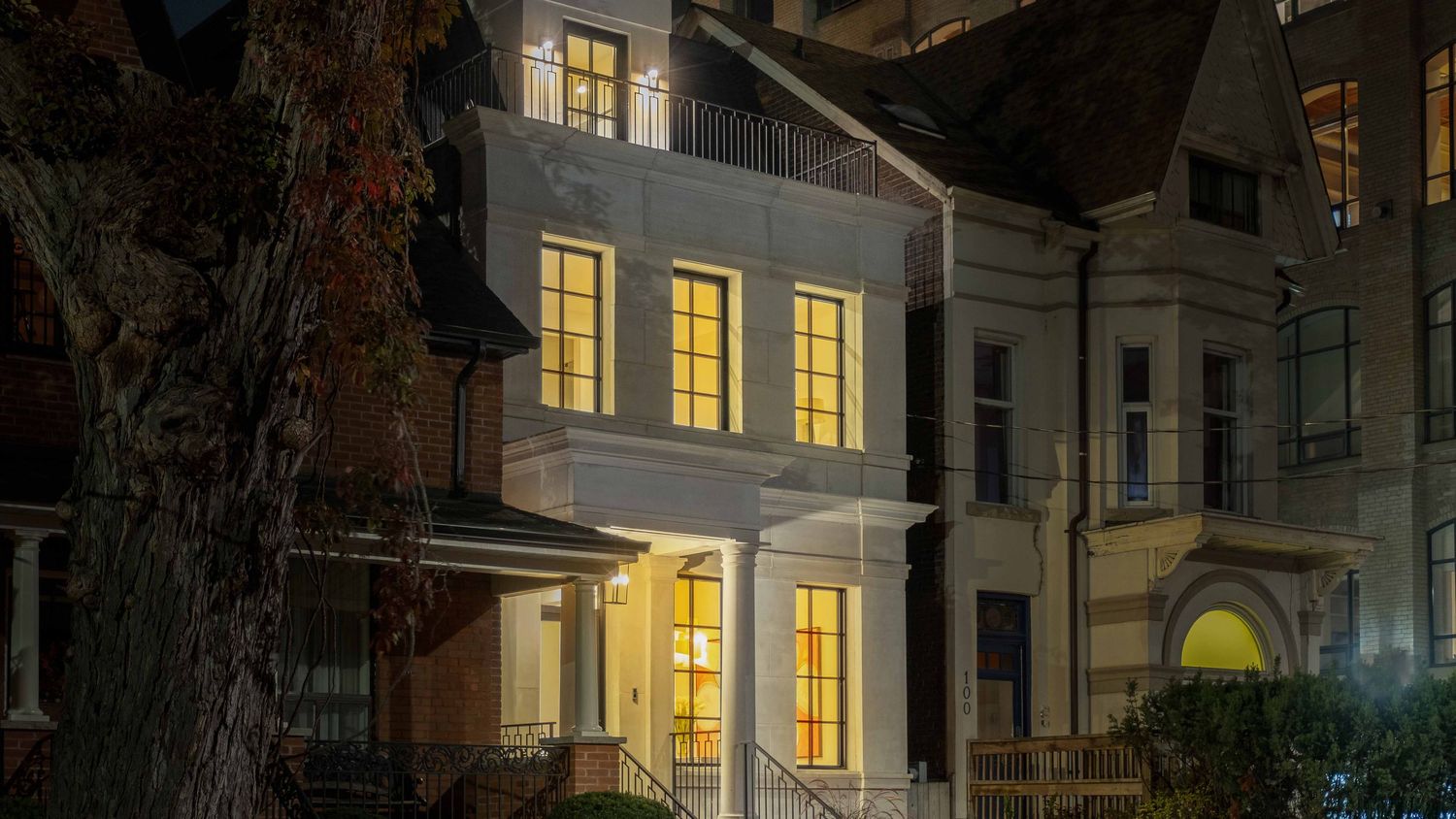 Historic row houses with glowing windows illuminate a quiet residential street at dusk.