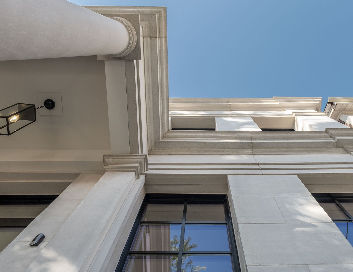 Security camera mounted on white exterior wall with window and blue sky visible.