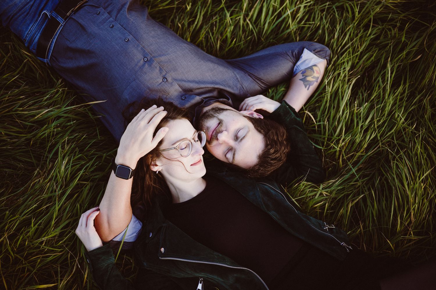 Person lying in green grass wearing dark clothing while looking at a mobile phone.