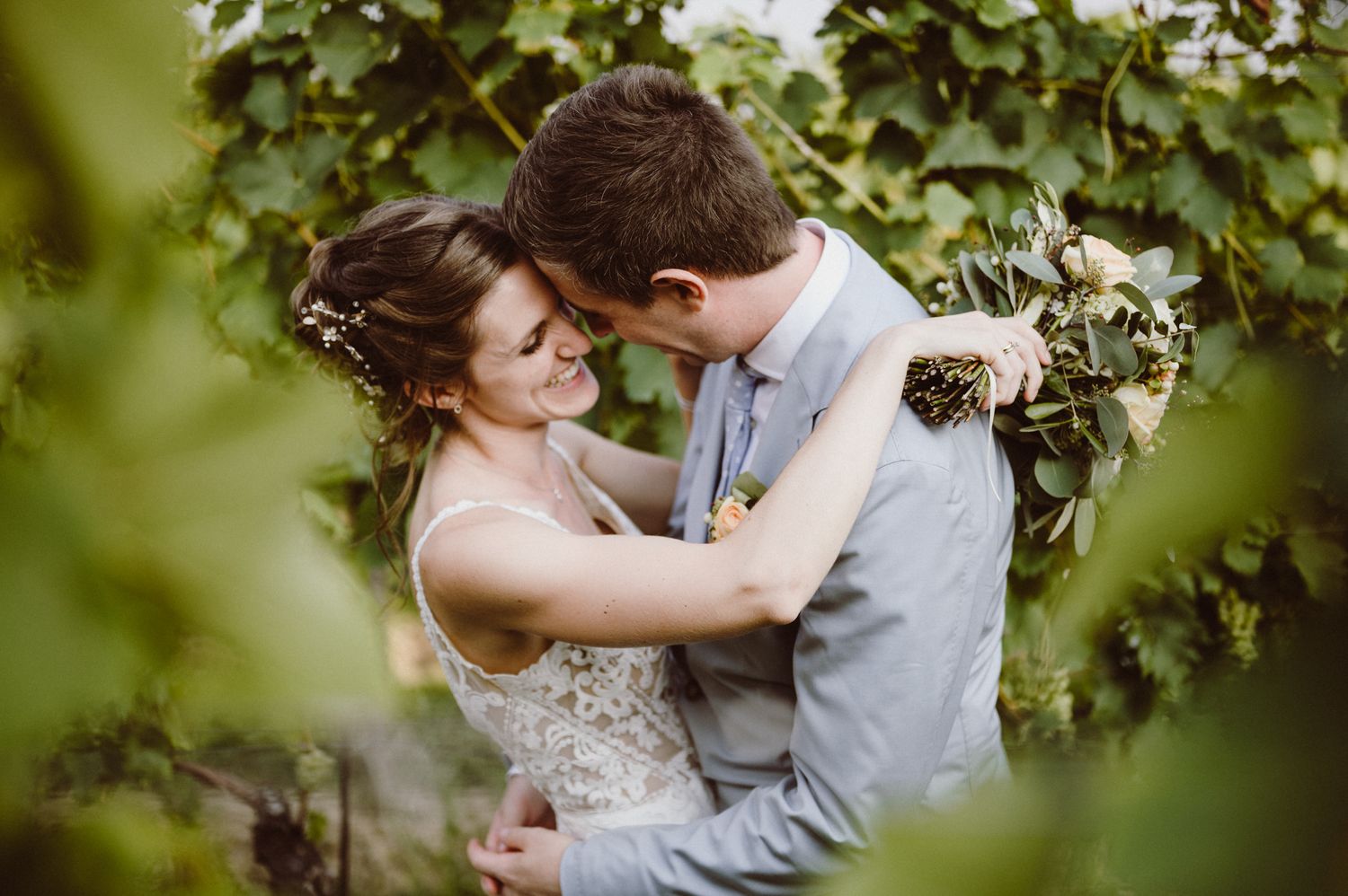 A romantic couple embraces in a garden setting surrounded by lush green foliage and natural light.