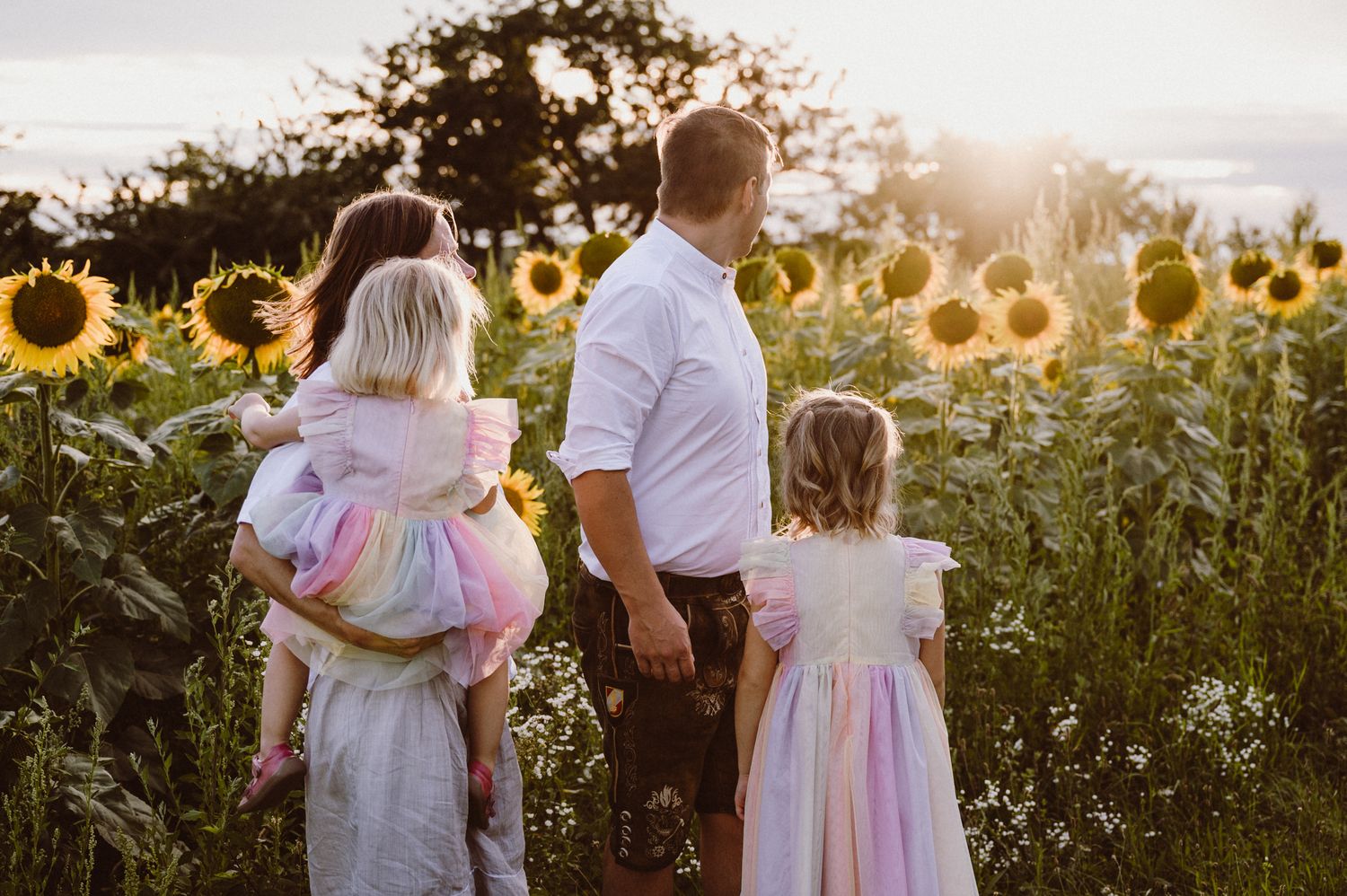 Family stands together admiring a beautiful golden sunflower field at sunset creating a magical silhouette.