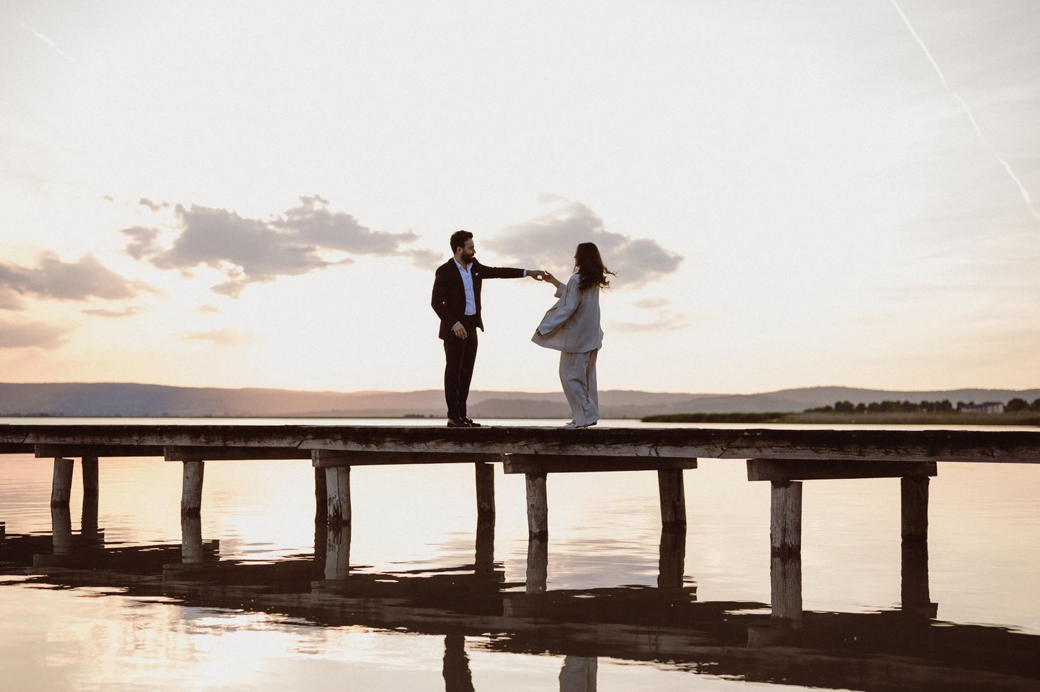 Silhouettes of people standing on a wooden pier at sunset creating a romantic and peaceful coastal atmosphere.