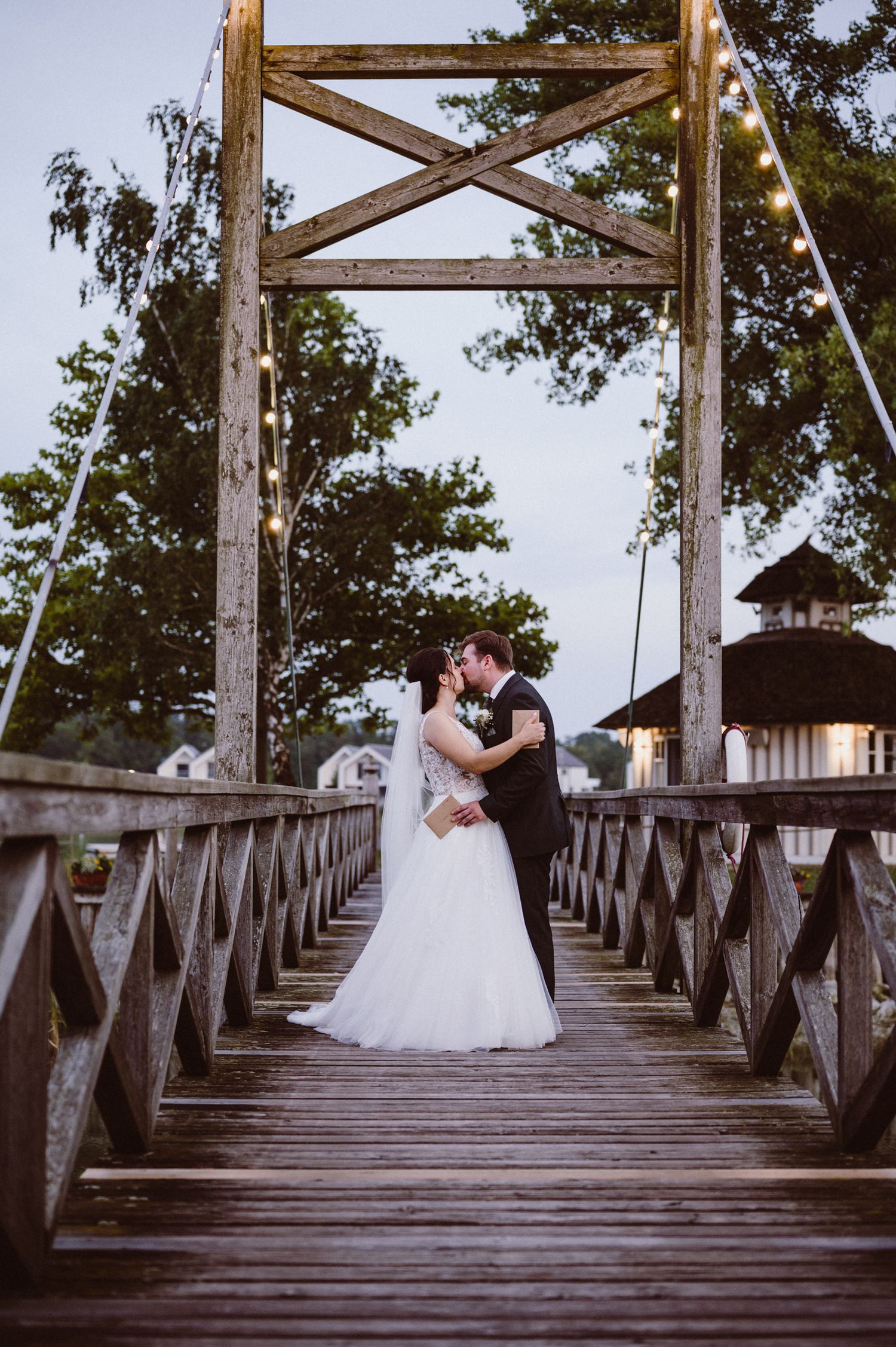 Romantic couple shares intimate moments on a wooden pier at dusk with string lights creating a magical atmosphere.