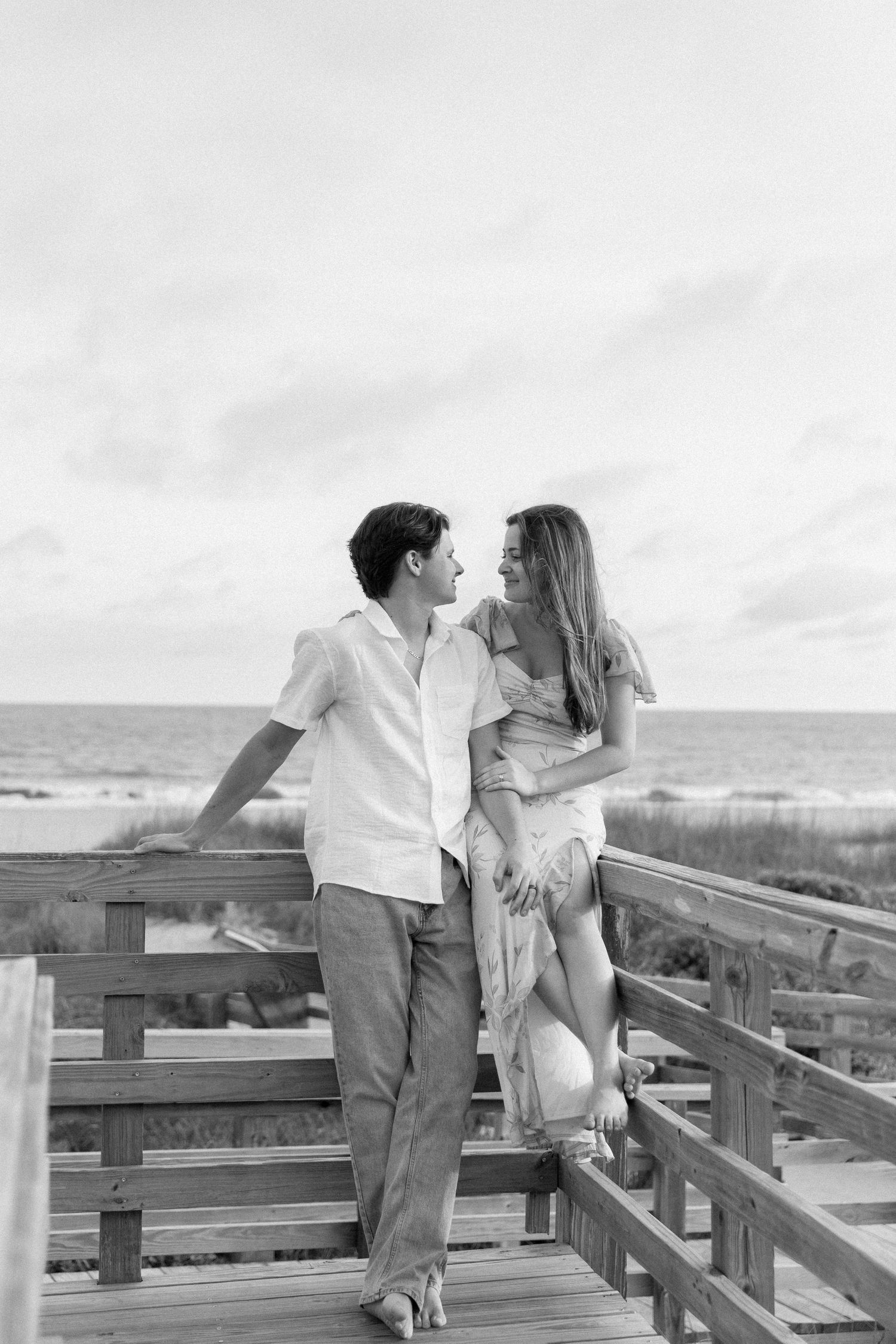 Black and white photo of a romantic couple embracing on a wooden boardwalk near the ocean beach.