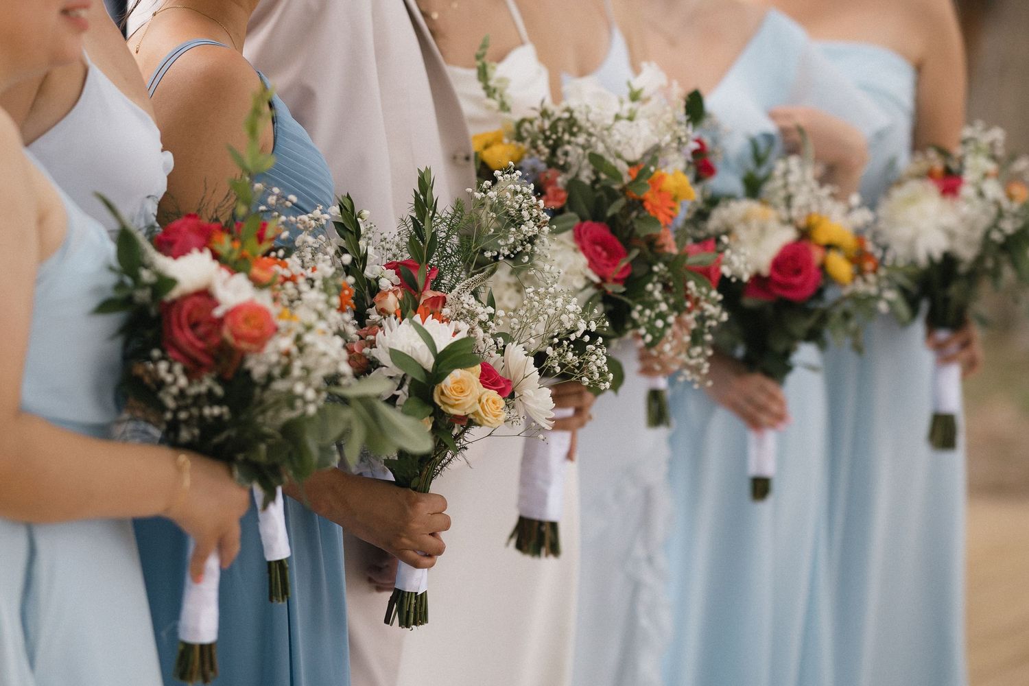 Bridesmaids in light blue dresses holding colorful wedding bouquets with roses and baby's breath.