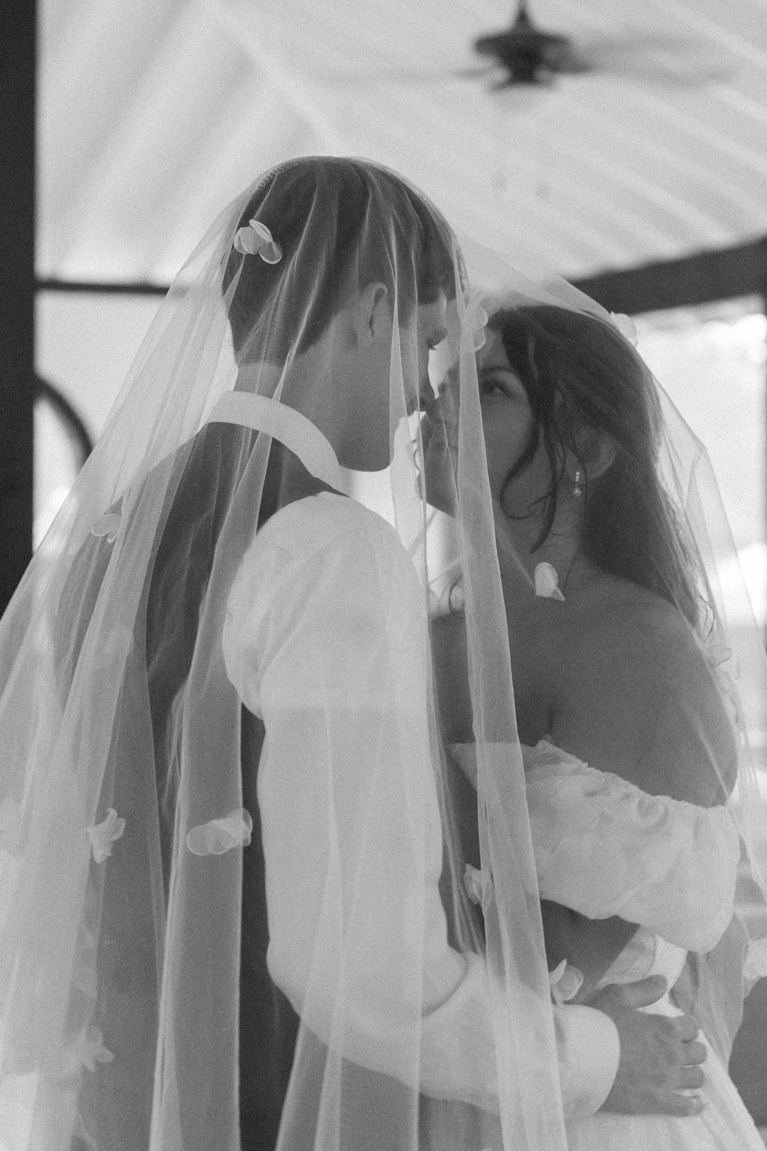 Black and white photo of bride and groom sharing intimate moment under wedding veil.