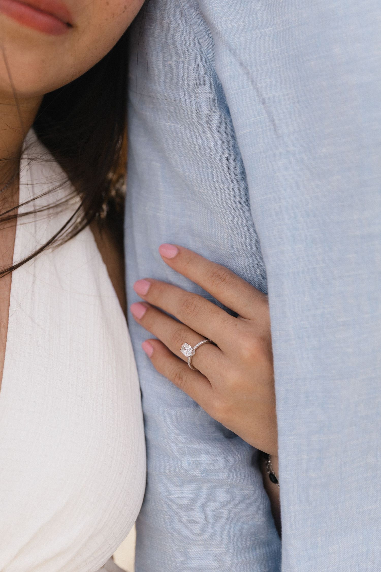 Close-up of a woman's hand with a diamond solitaire engagement ring resting on a man's blue linen jacket.
