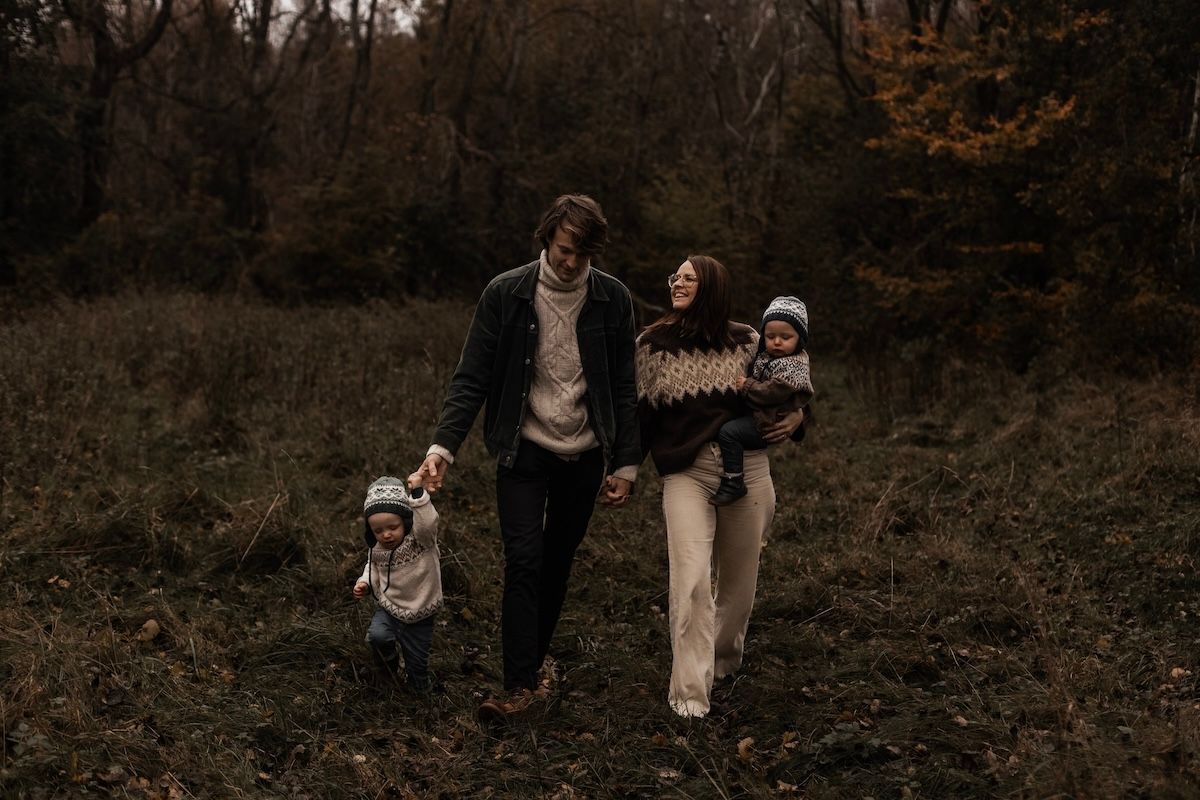 En familj håller händer och går genom skogen under en familjefotografering i Skåne. Foto: Grevholm Photography.